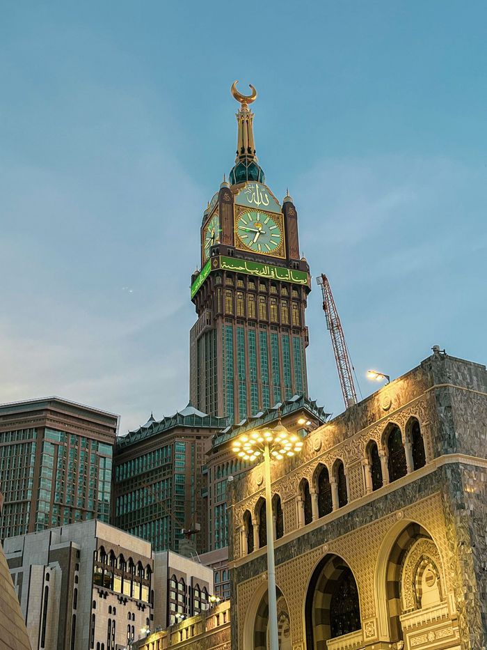 A clock tower with a statue on top of it is in the middle of a city.