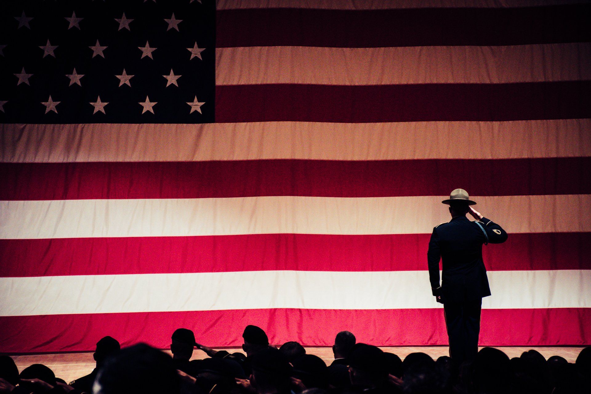 a man in a hat is saluting in front of an american flag .