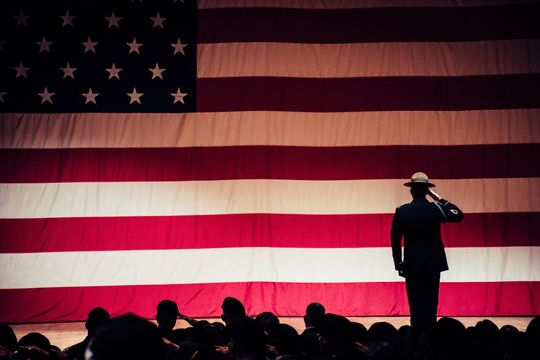 A man in a hat is saluting in front of an american flag.