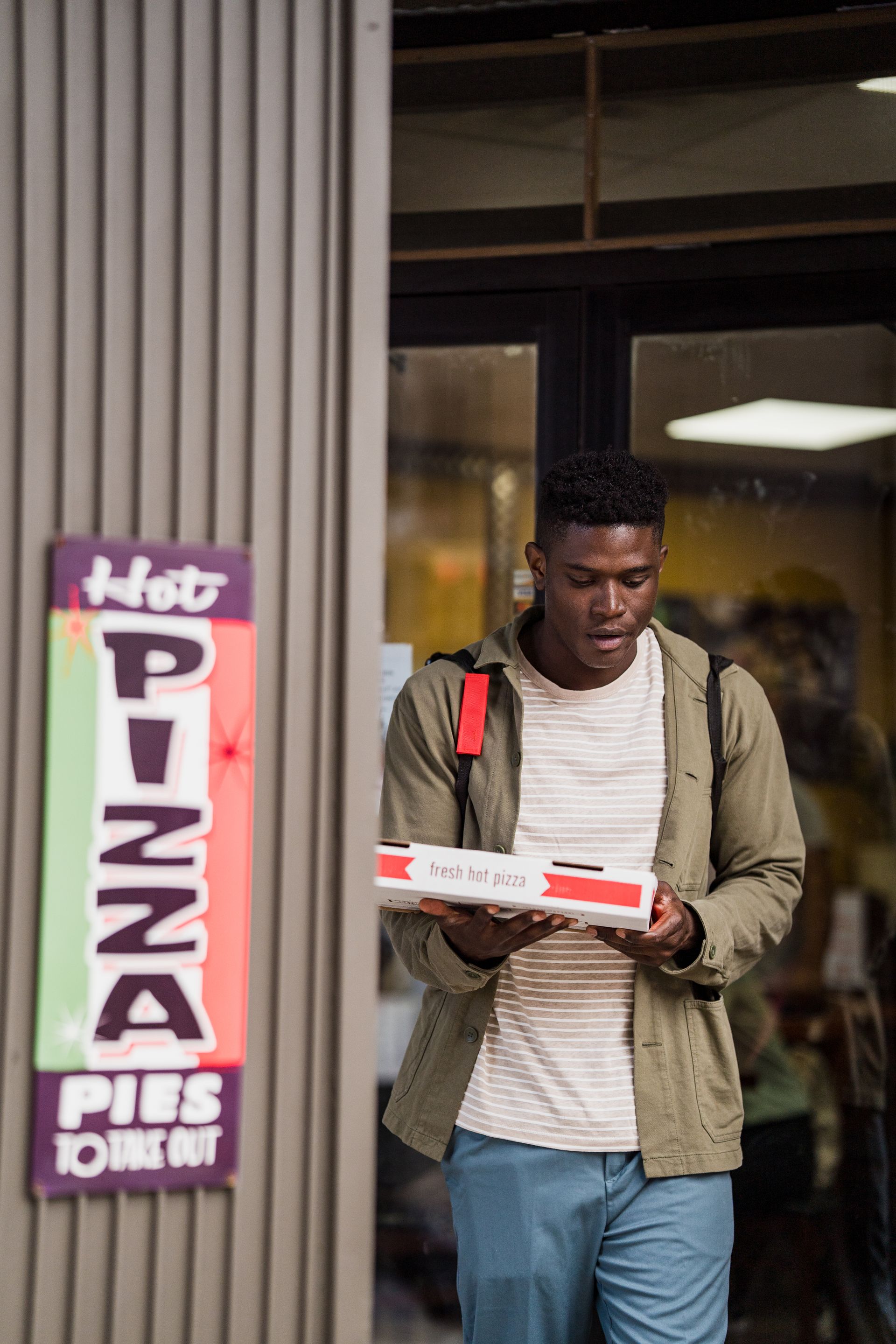 A man is holding a pizza box in front of a pizza restaurant.