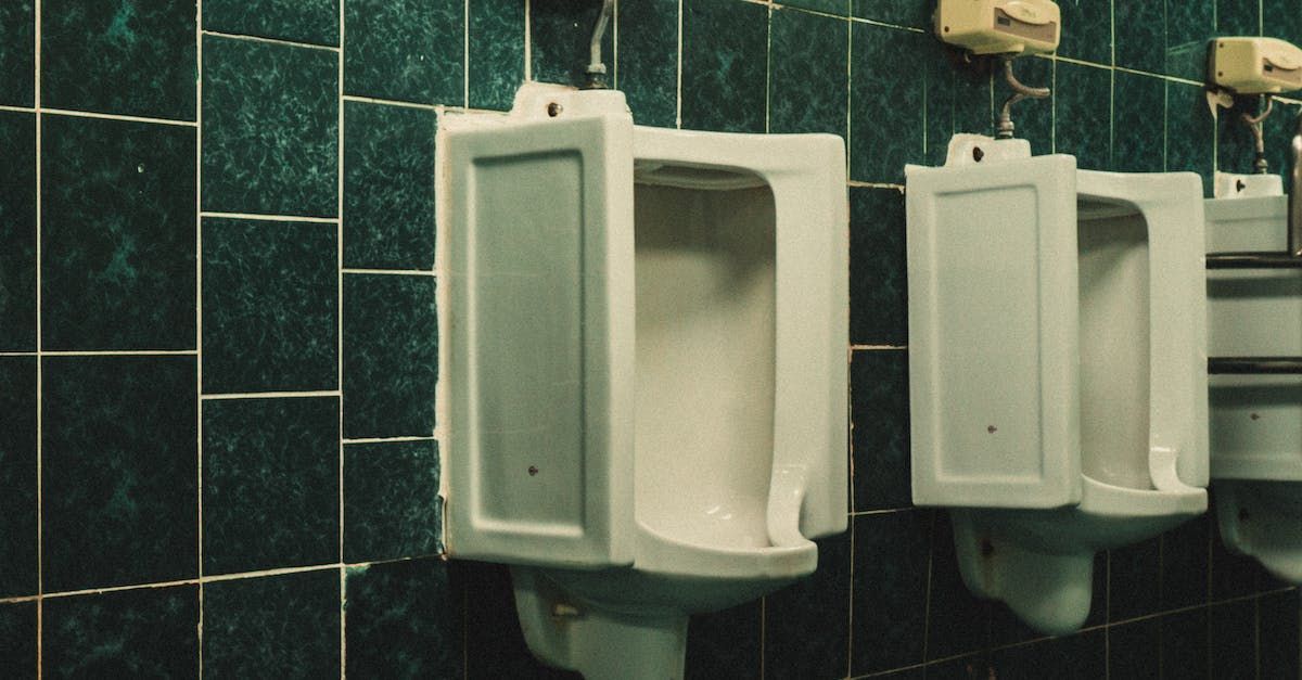 A row of urinals in a bathroom with green tiles