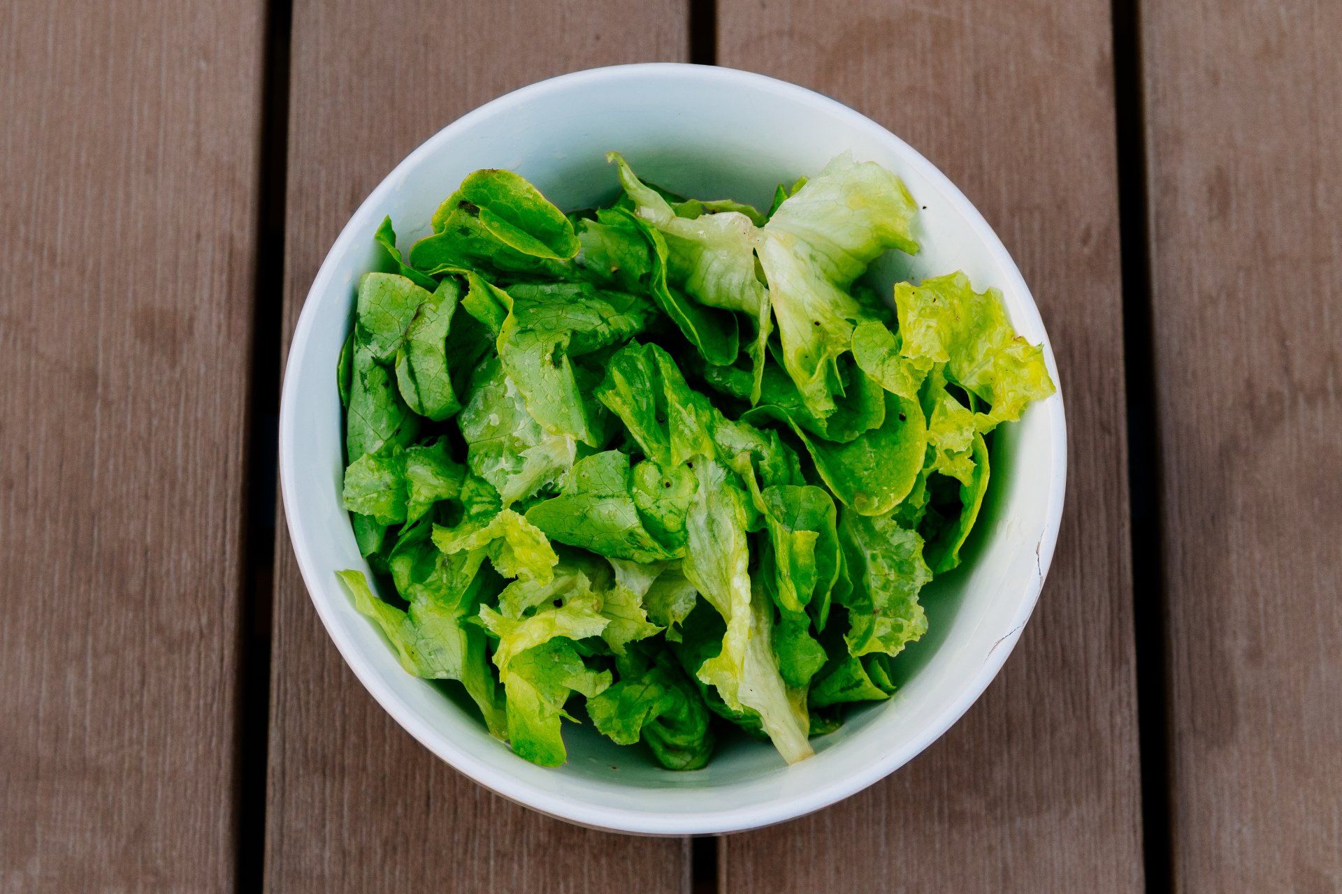 A bowl of lettuce is sitting on a wooden table.