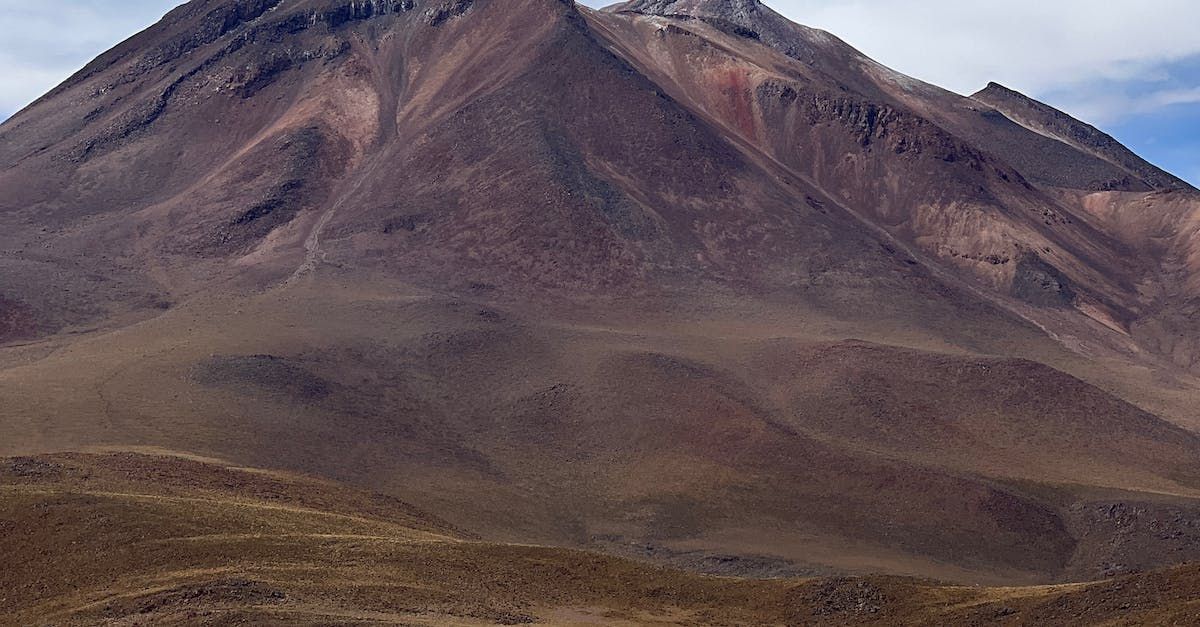 Montaña rocosa de color marrón, con una cima oscura, contra un cielo azul, en un paisaje desolado.