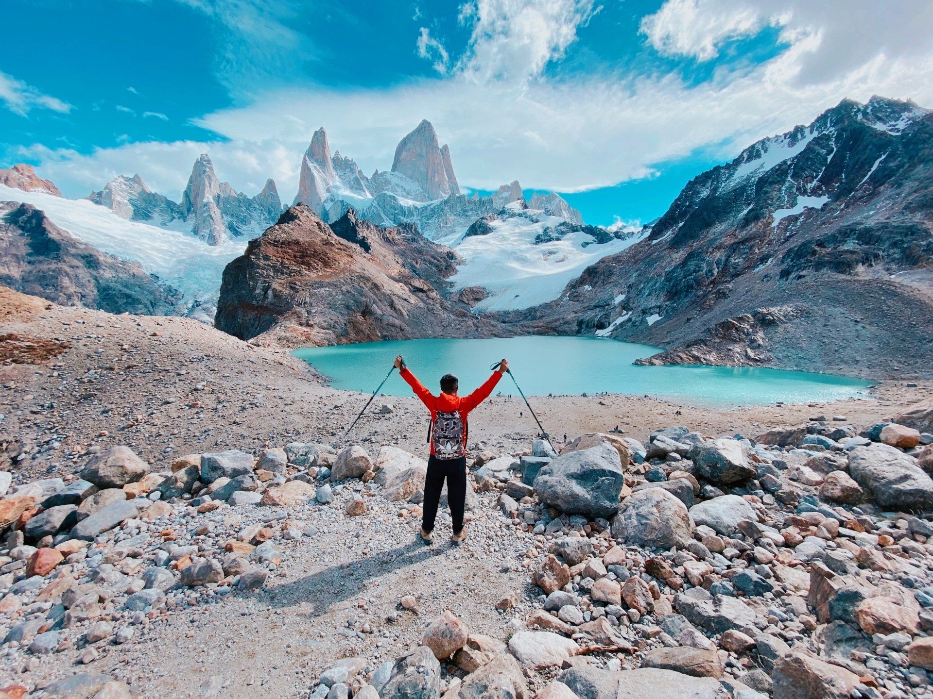 A man is standing in front of a lake in the mountains with his arms outstretched.