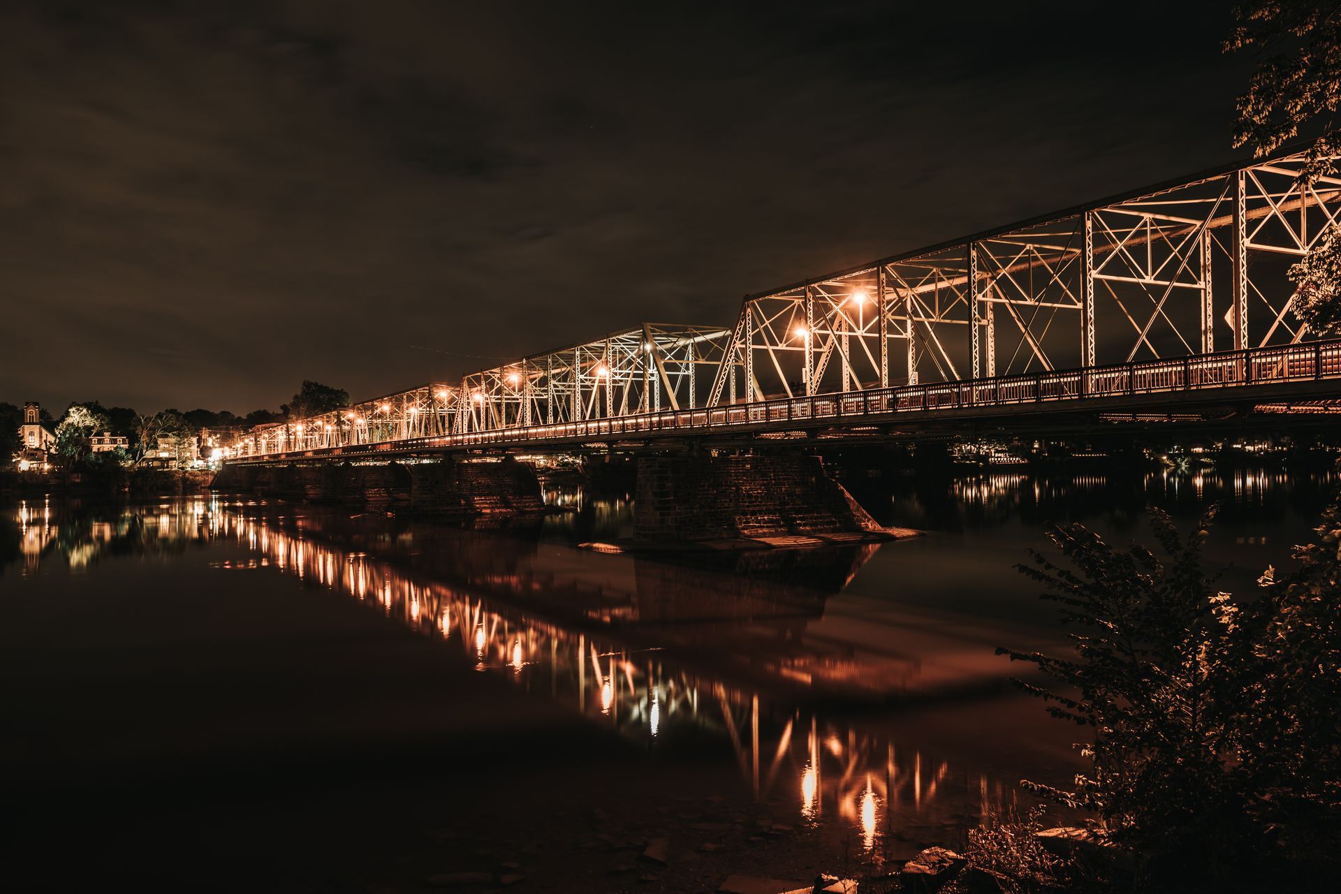 A bridge over a river at night with lights reflected in the water.