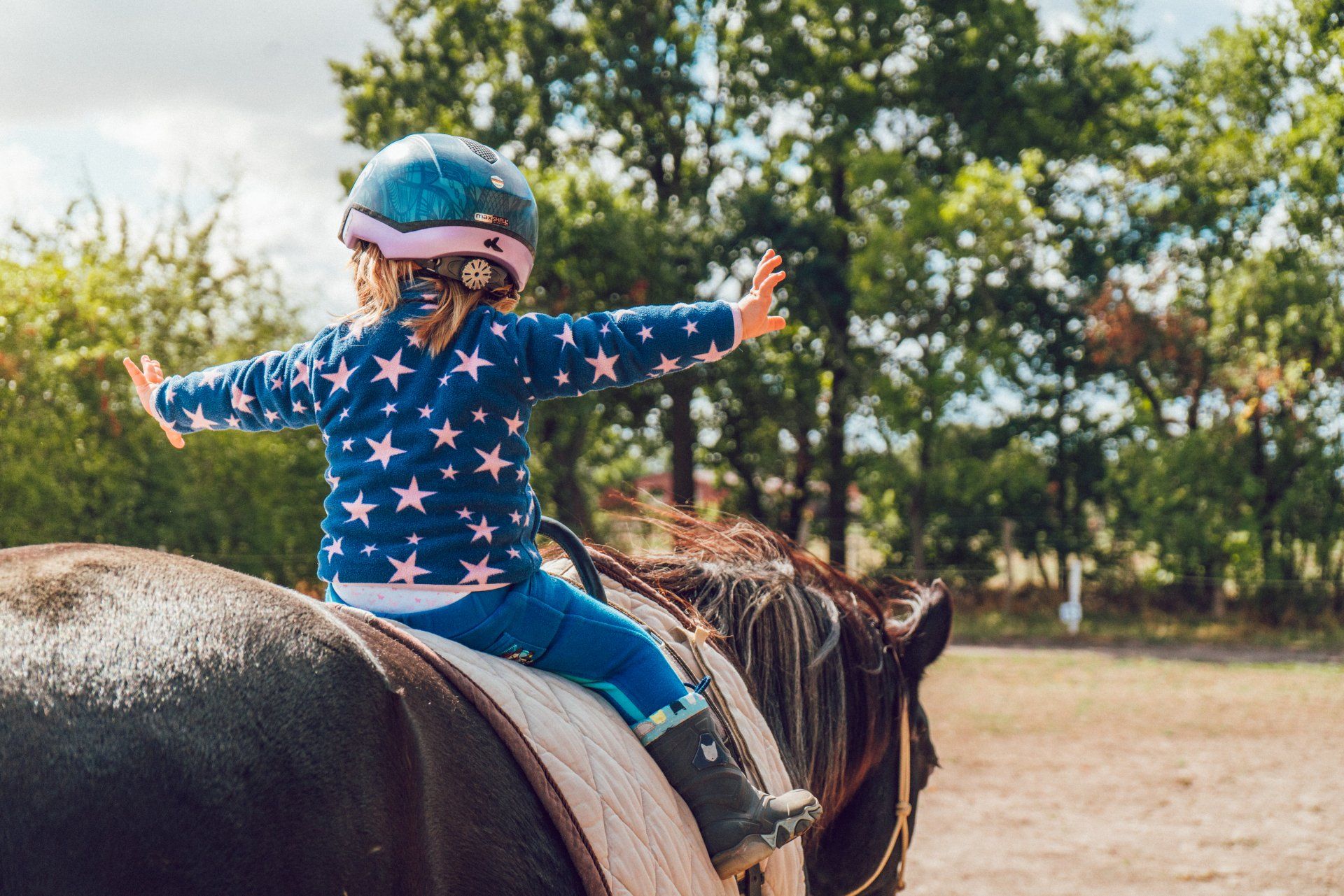 a little girl is riding a horse with her arms outstretched .