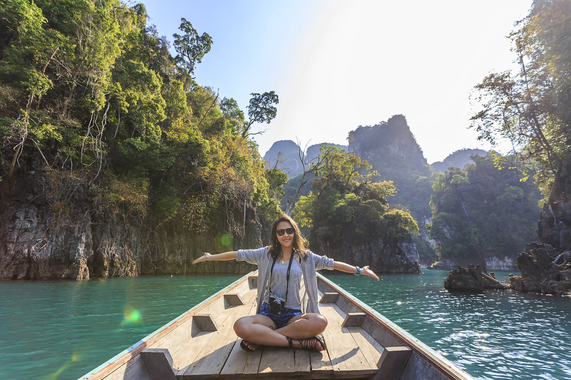 Una mujer está sentada en un bote en un lago con los brazos extendidos.