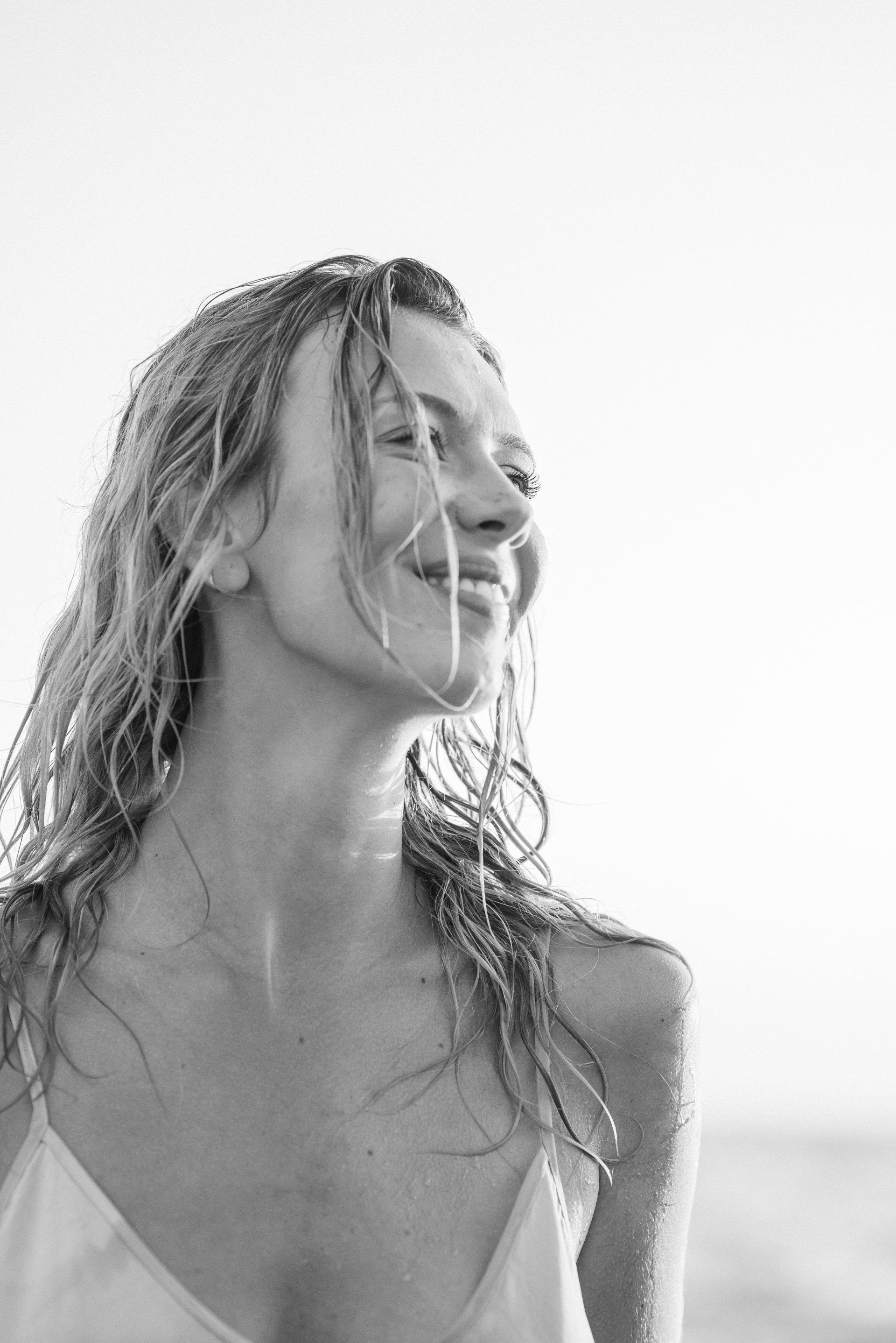 A black and white photo of a woman smiling on the beach.