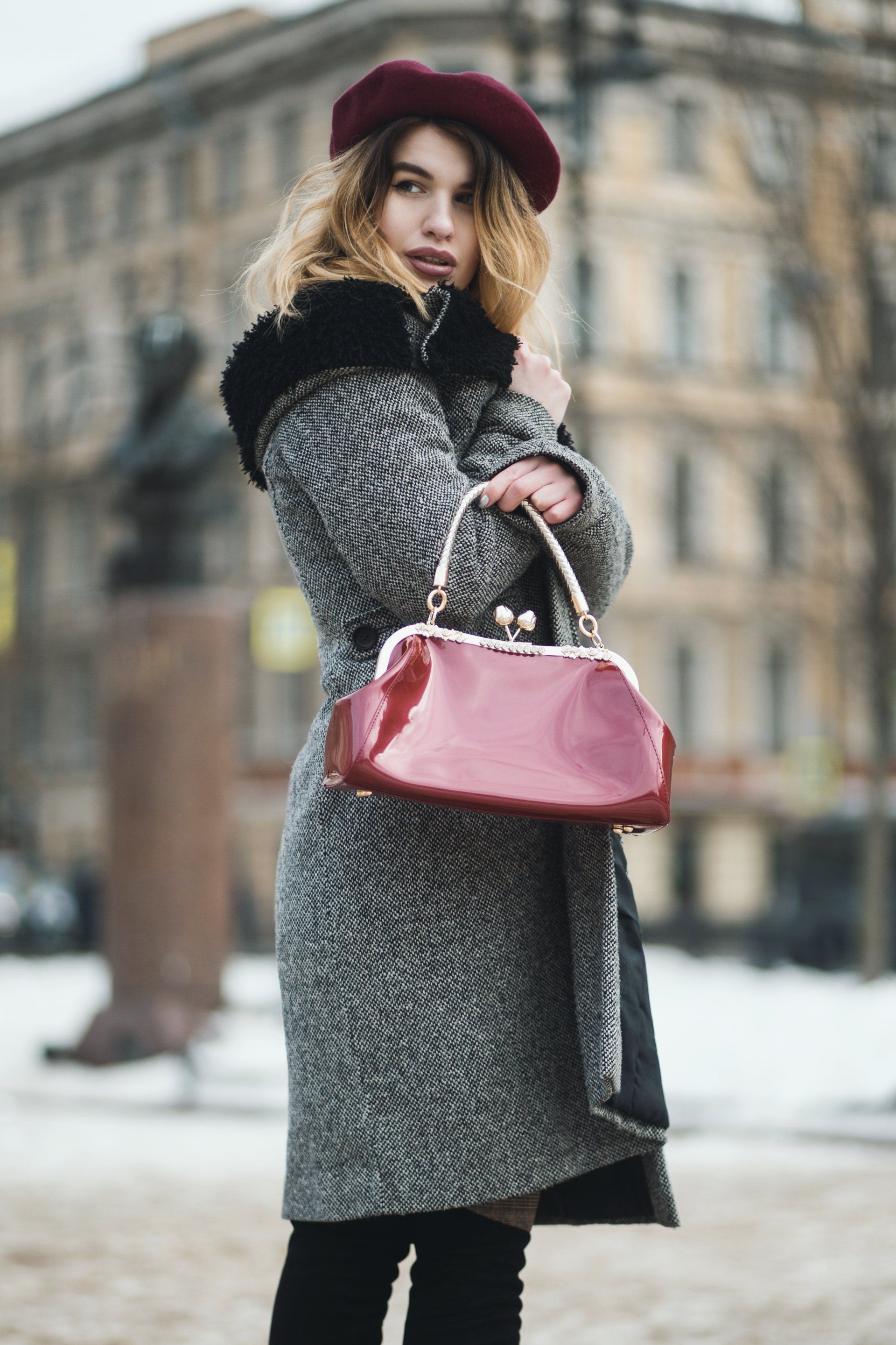 A woman in a coat and beret is holding a red purse.