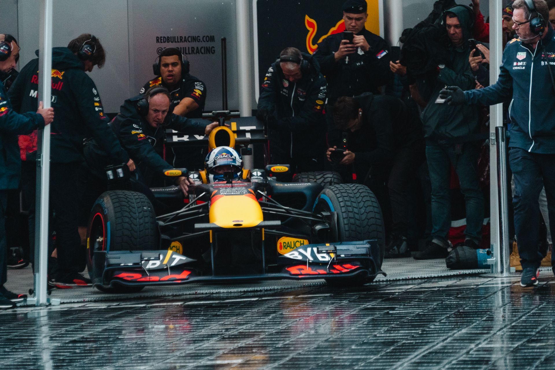 A group of people are standing around a race car in a garage.