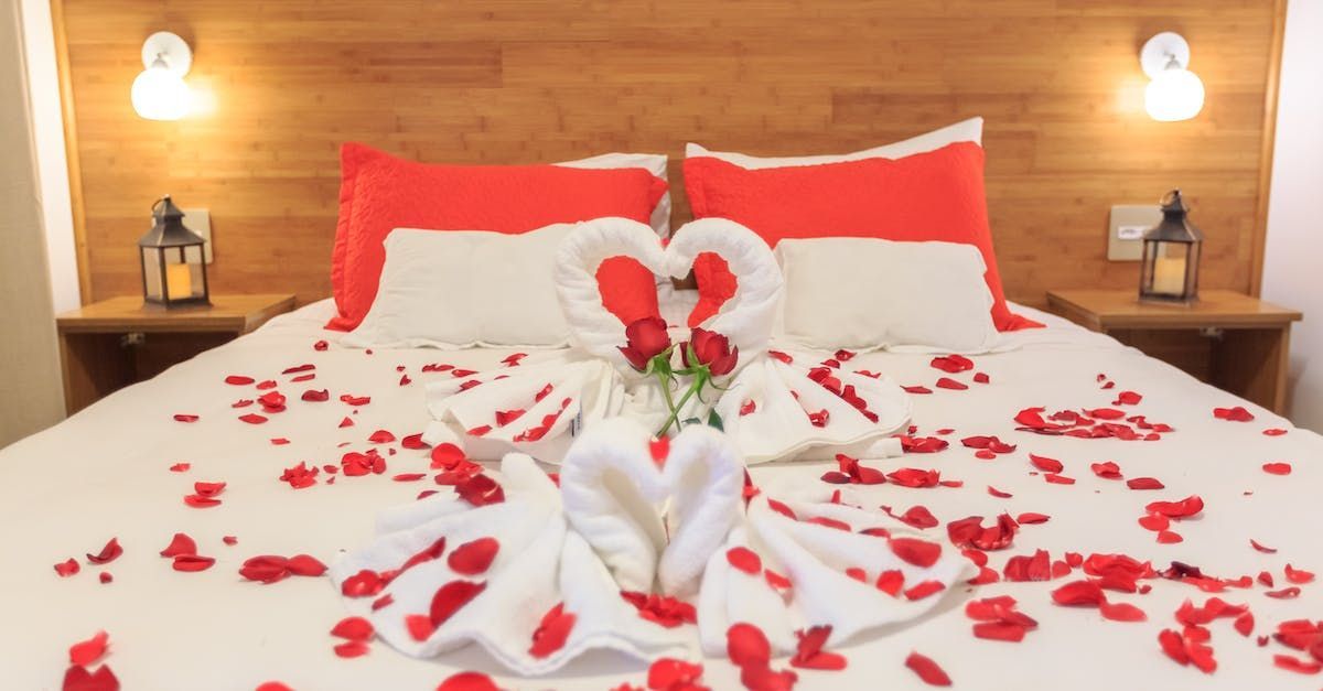 uma cama decorada para o dia dos namorados com rosas e toalhas em formato de cisnes.