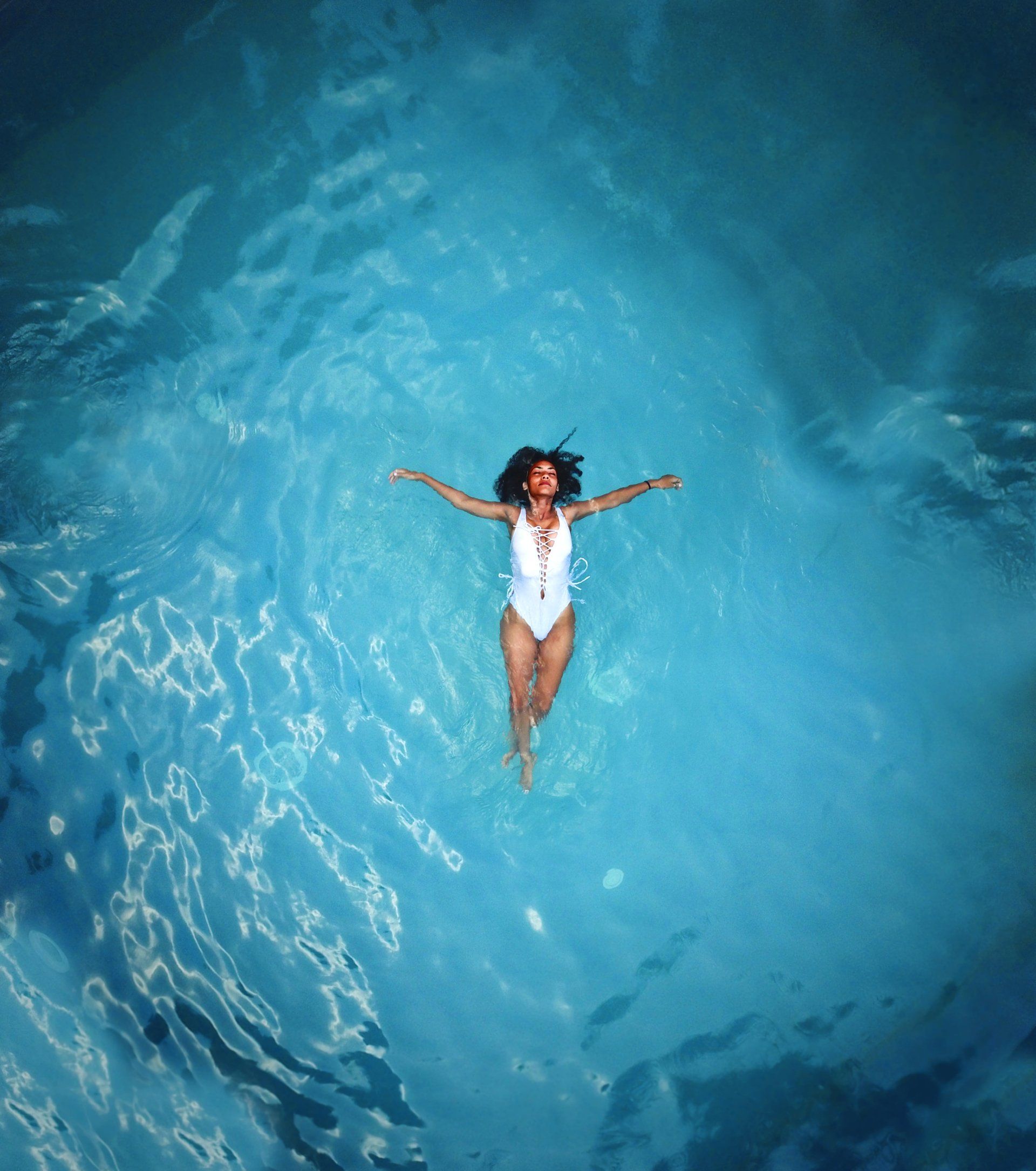 A lady in a white bathing suit in blue open water doing backstroke