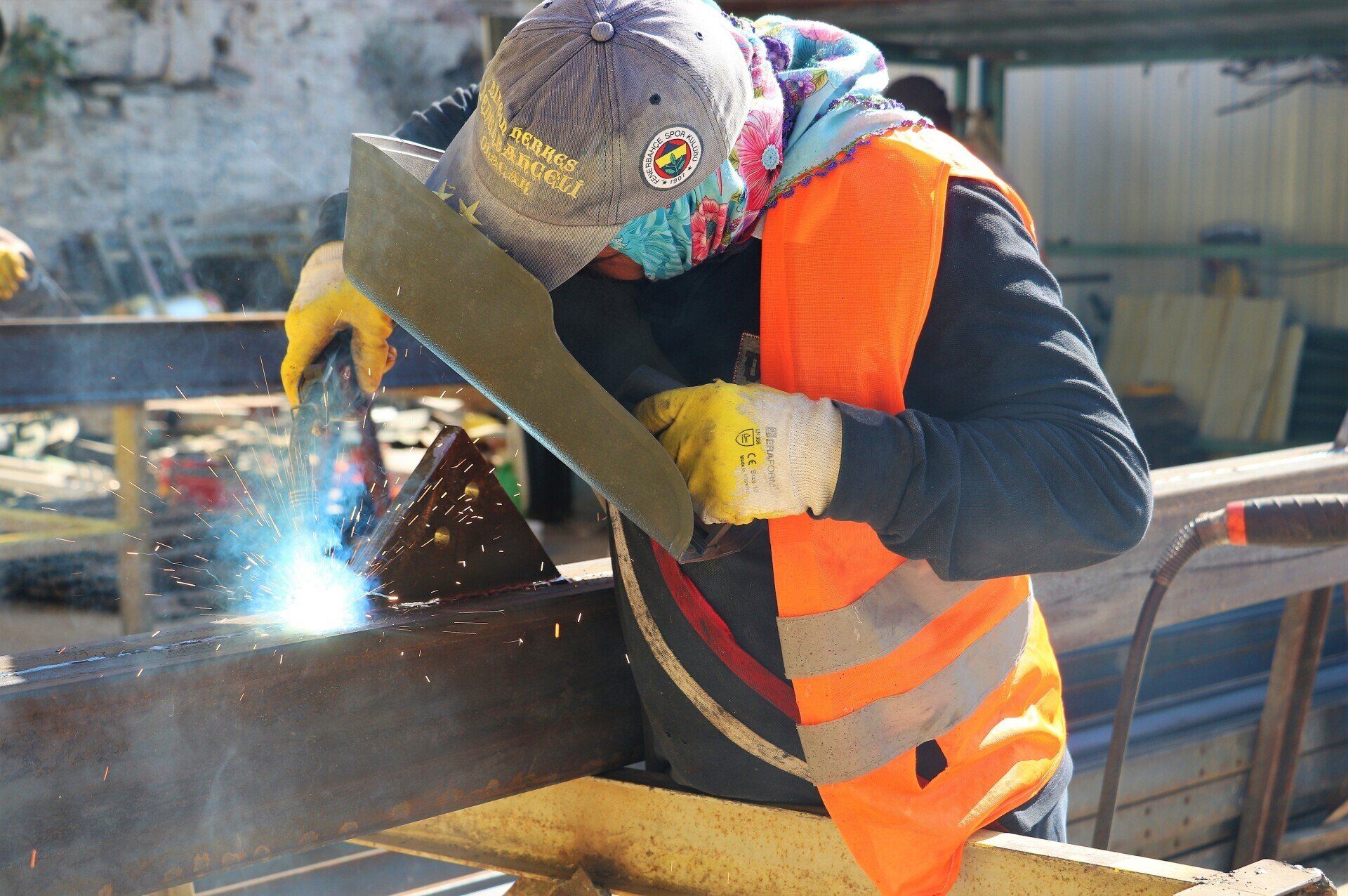 A Man Wearing an Orange Vest is Welding a Piece of Metal — NQBC Pty Ltd in Bowen, QLD