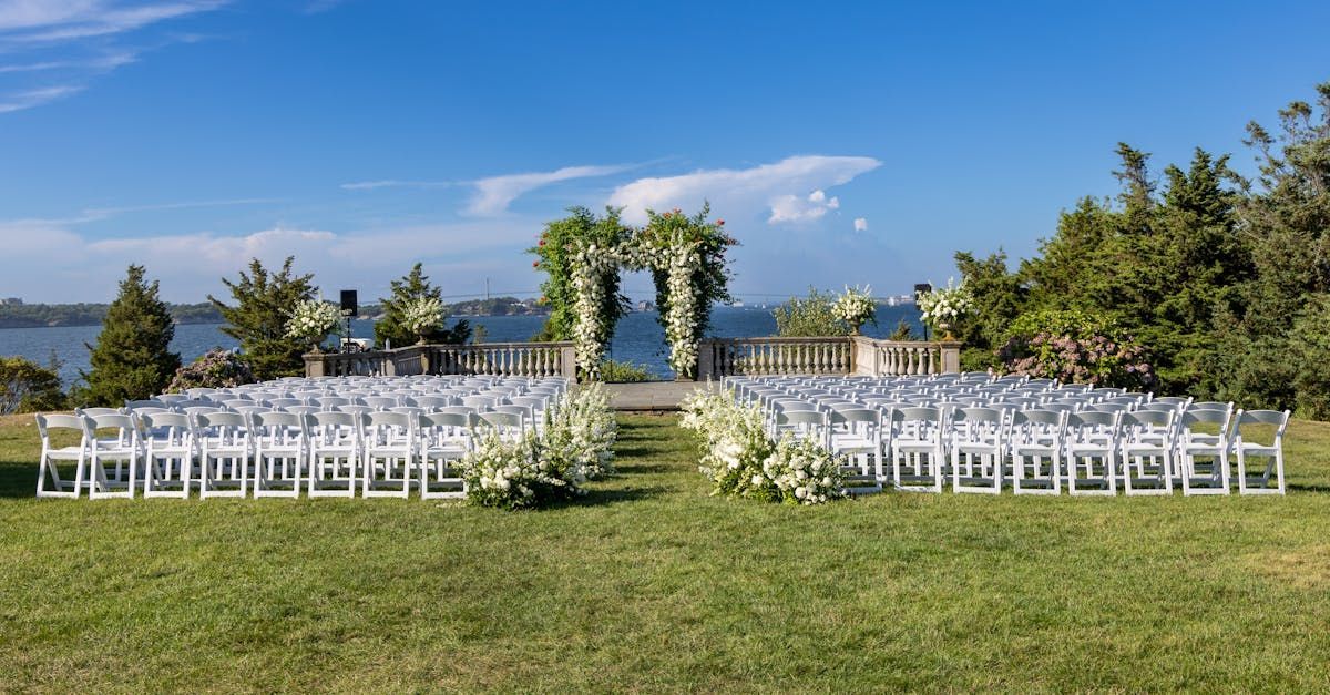 A row of white chairs are lined up in a grassy field for a wedding ceremony.