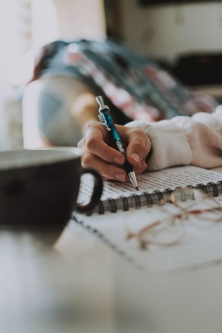 A person is writing in a notebook next to a cup of coffee.