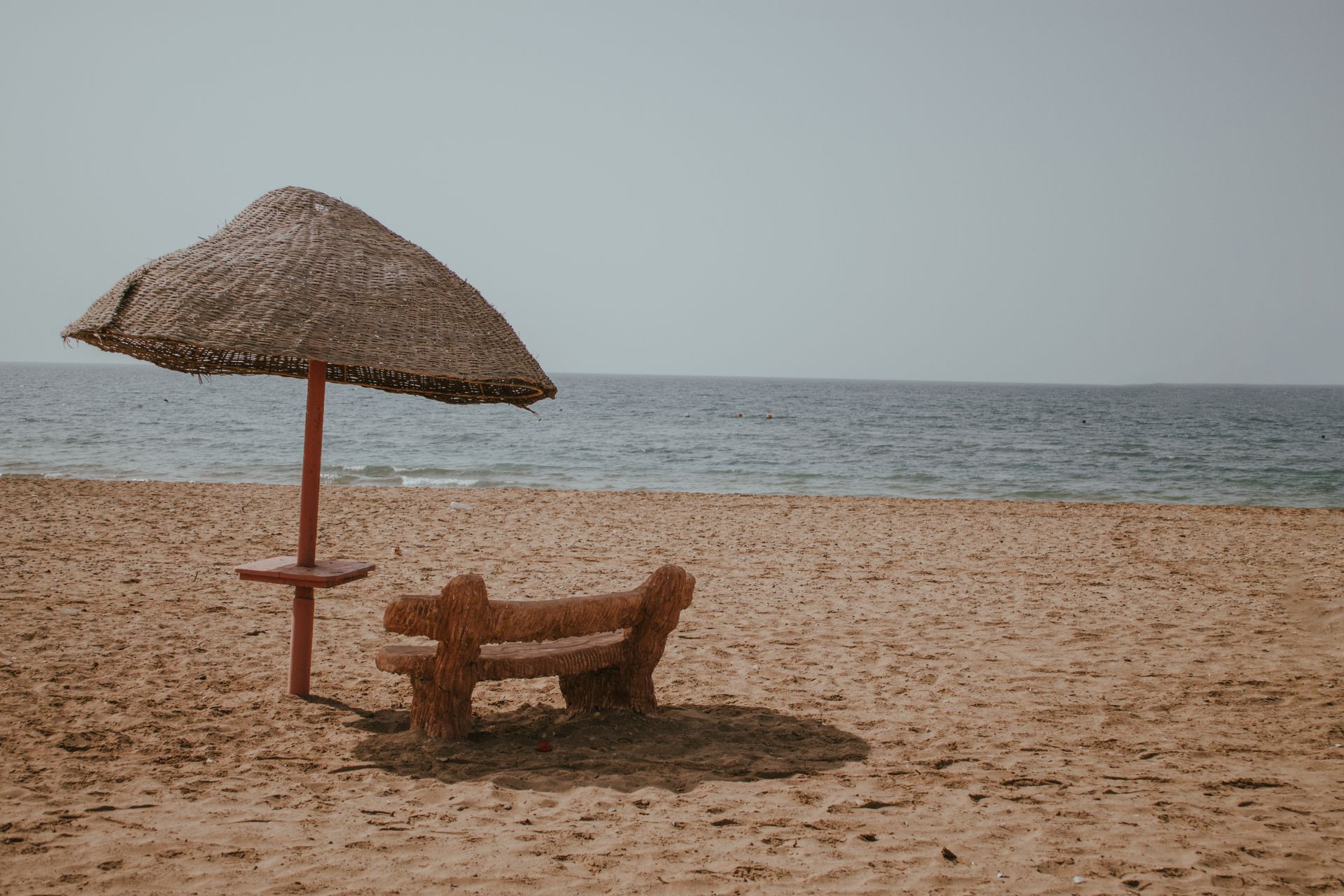There is a bench and an umbrella on the beach.
