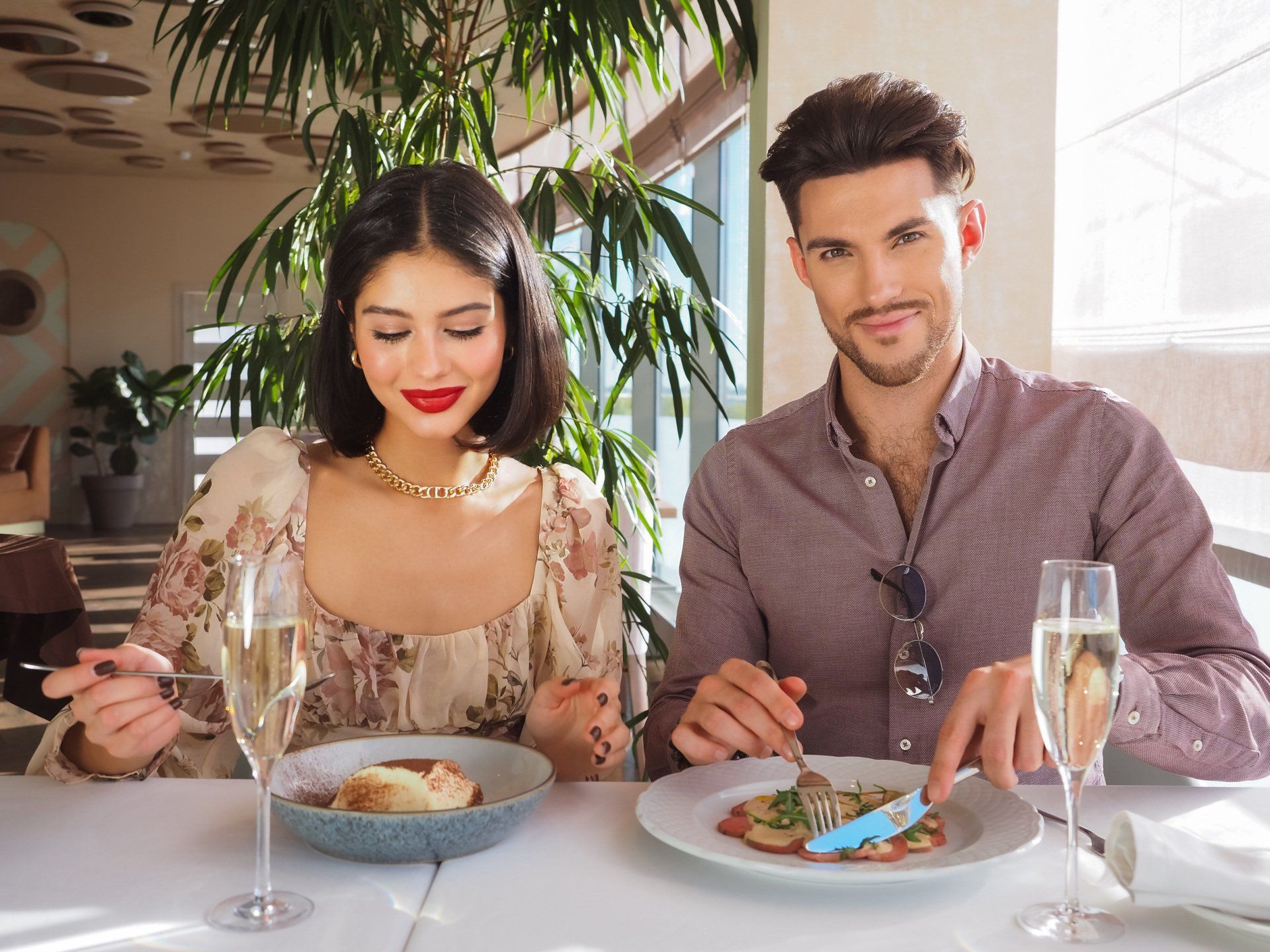 A man and a woman are sitting at a table eating food and drinking champagne.