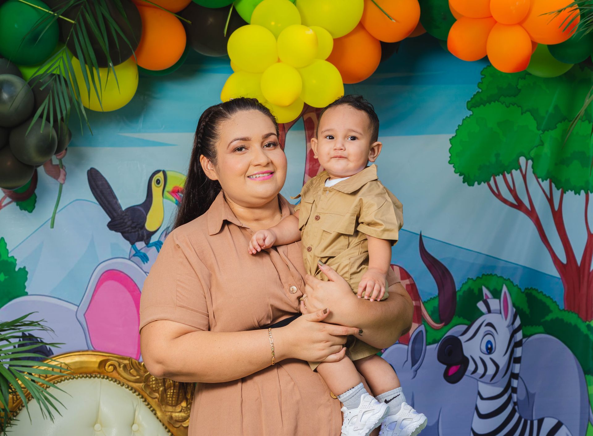 A woman is holding a baby in her arms in front of a jungle background.