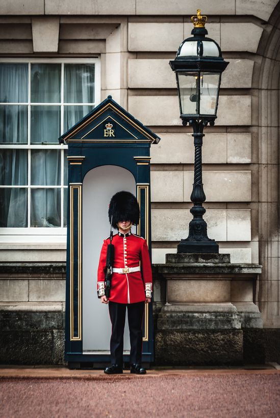 A soldier in a red uniform is standing in front of a building.