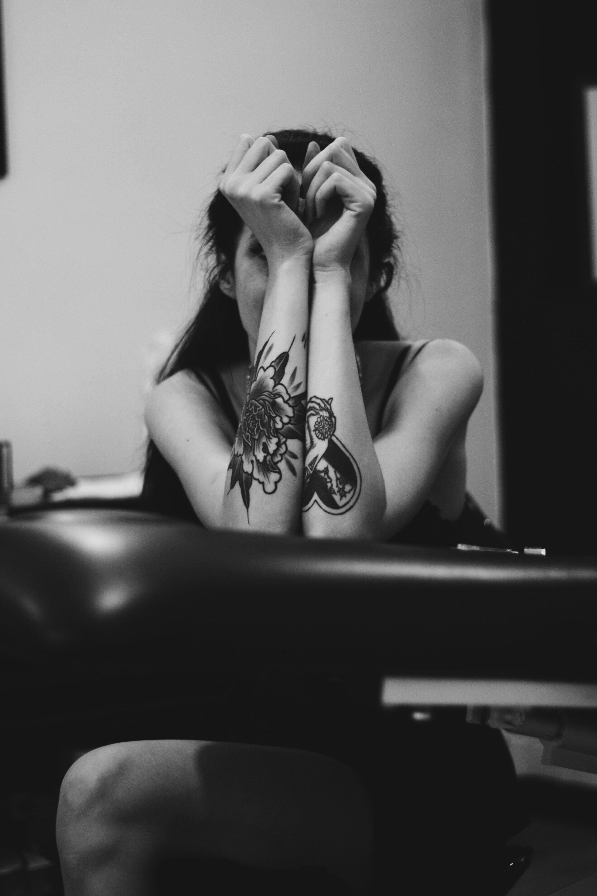 A woman with a tattoo on her arm is covering her face with her hands