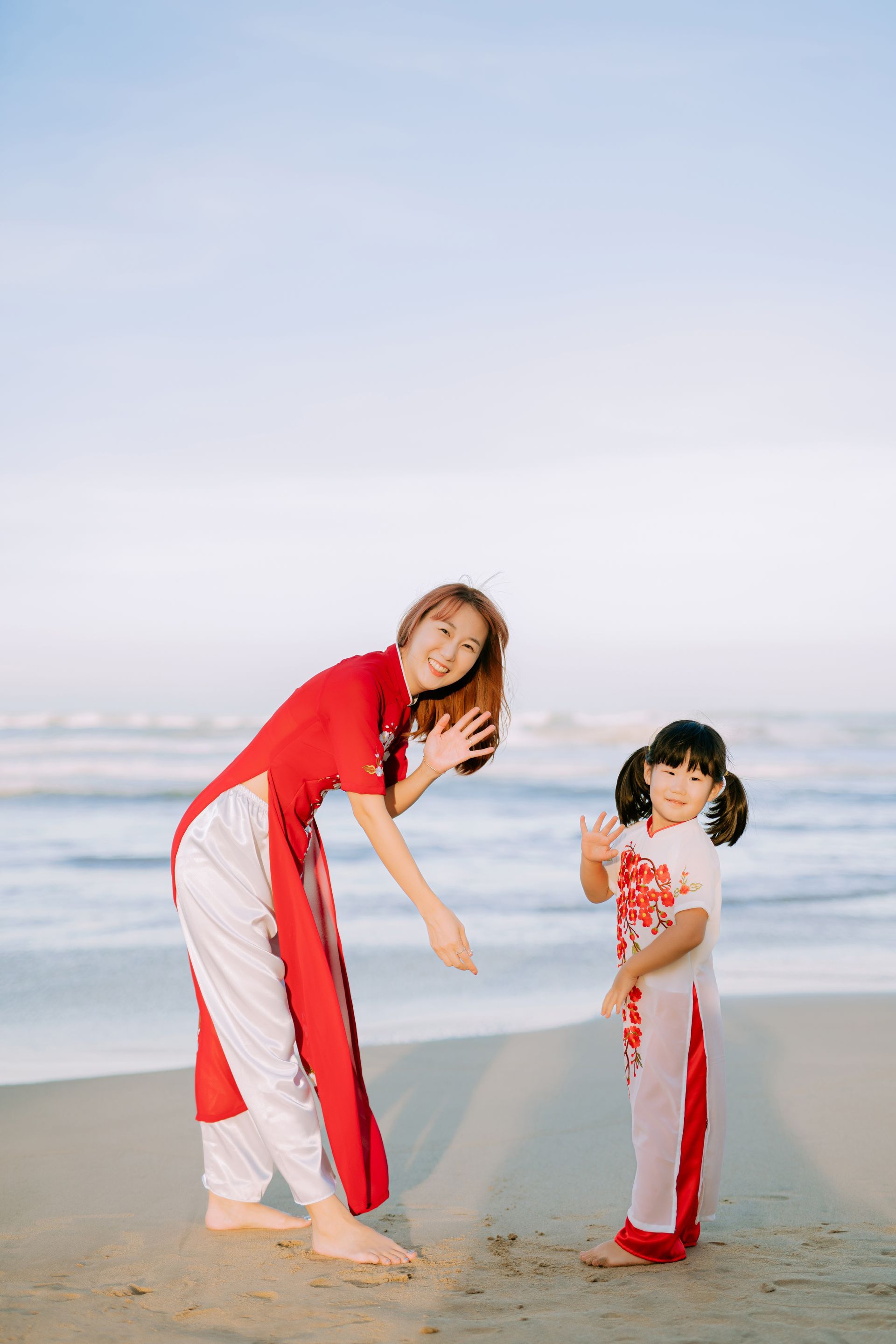 A woman and a little girl are posing for a picture on the beach.
