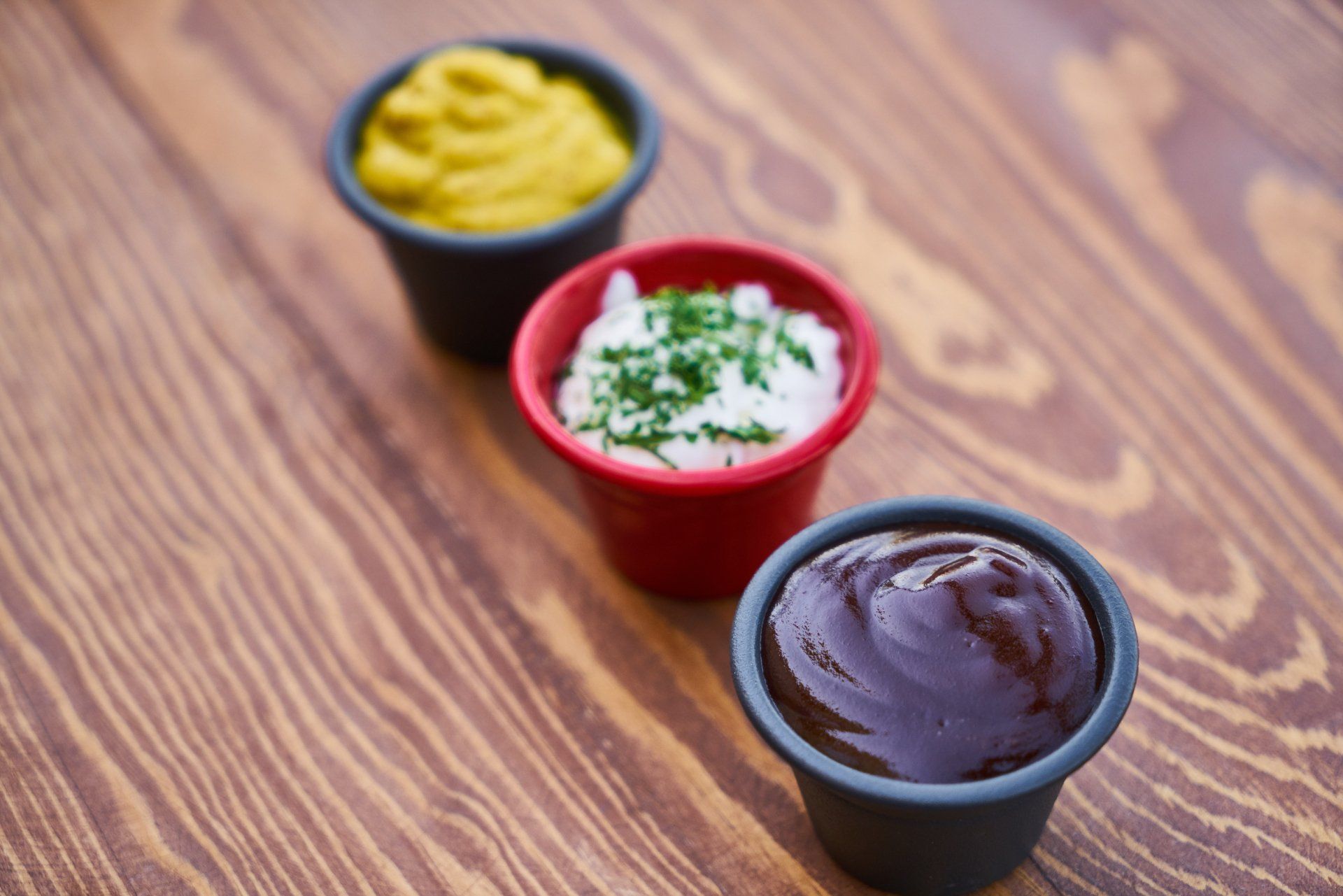 Three small bowls of different sauces are on a wooden table.