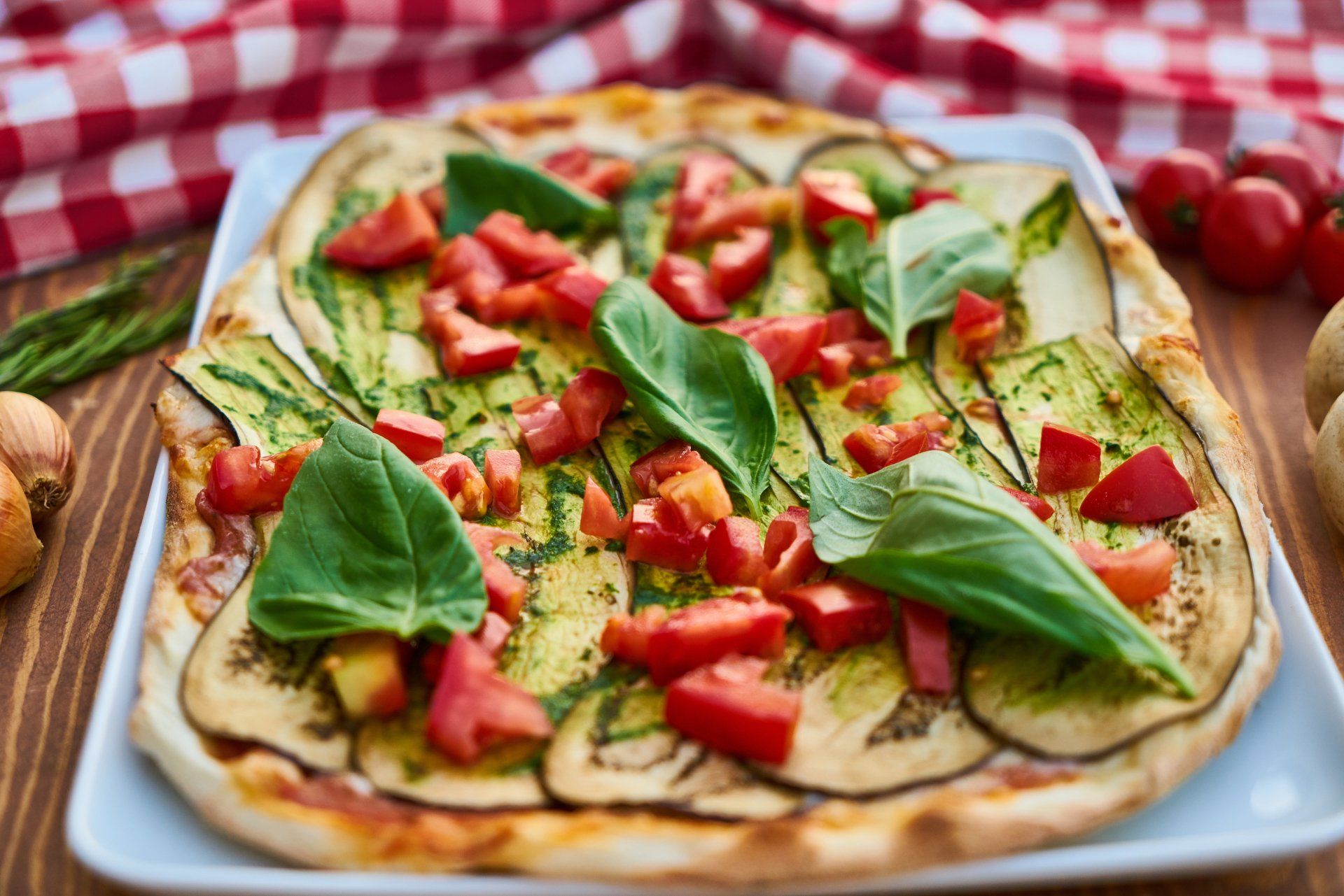 A pizza with tomatoes , zucchini and basil on a white plate on a wooden table.