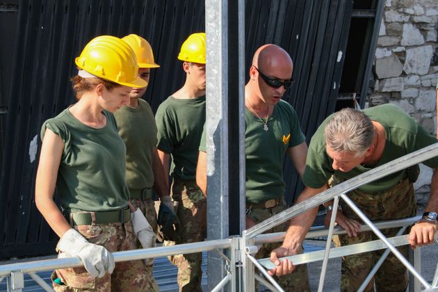 A group of soldiers wearing hard hats are working on a metal structure.
