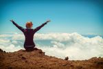 A woman is sitting on top of a mountain with her arms outstretched.