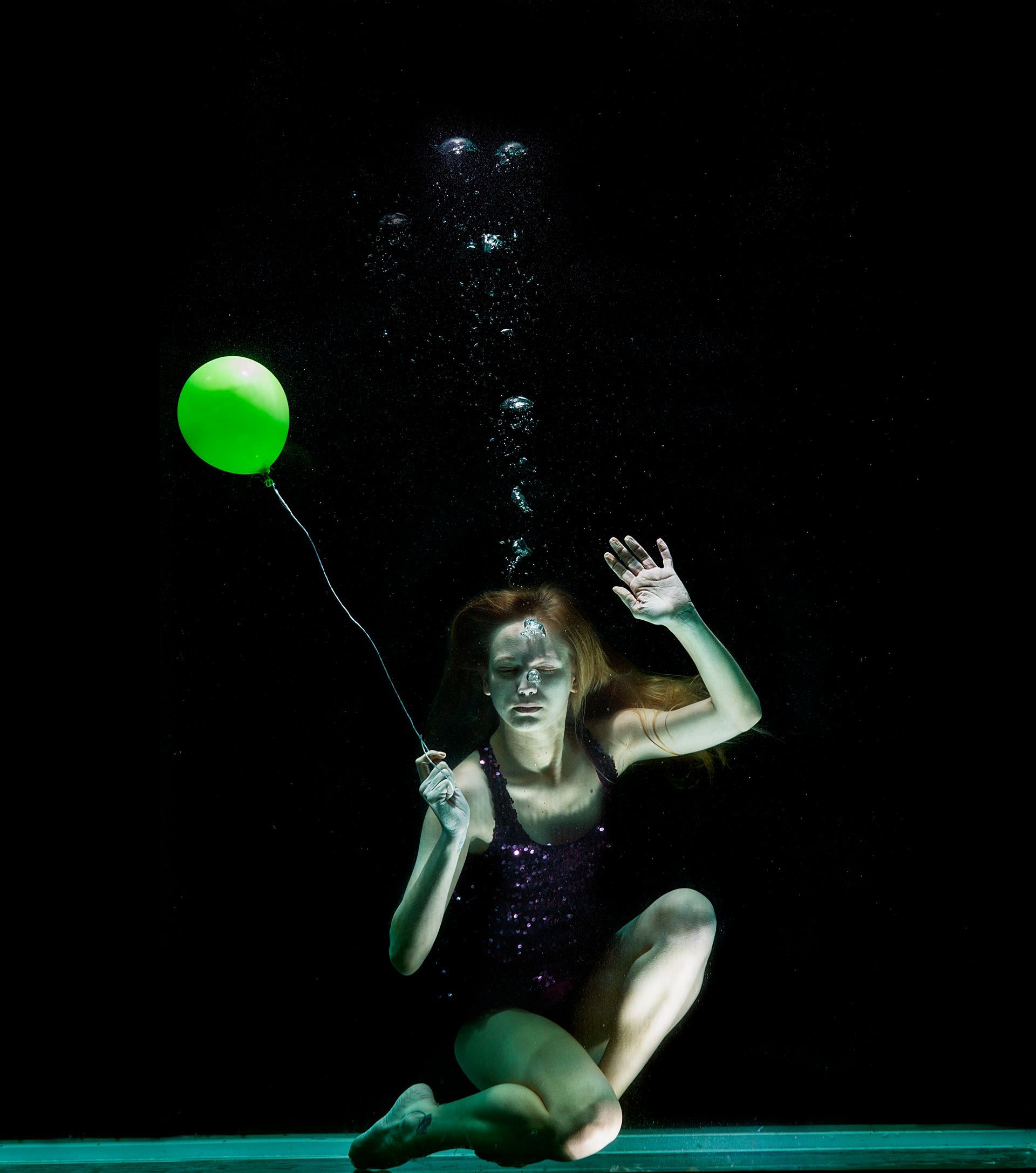 Girl underwater blowing bubbles of breath, holding a balloon