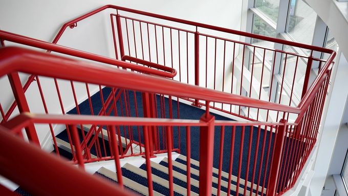 A red railing on a set of stairs with a blue and white rug.