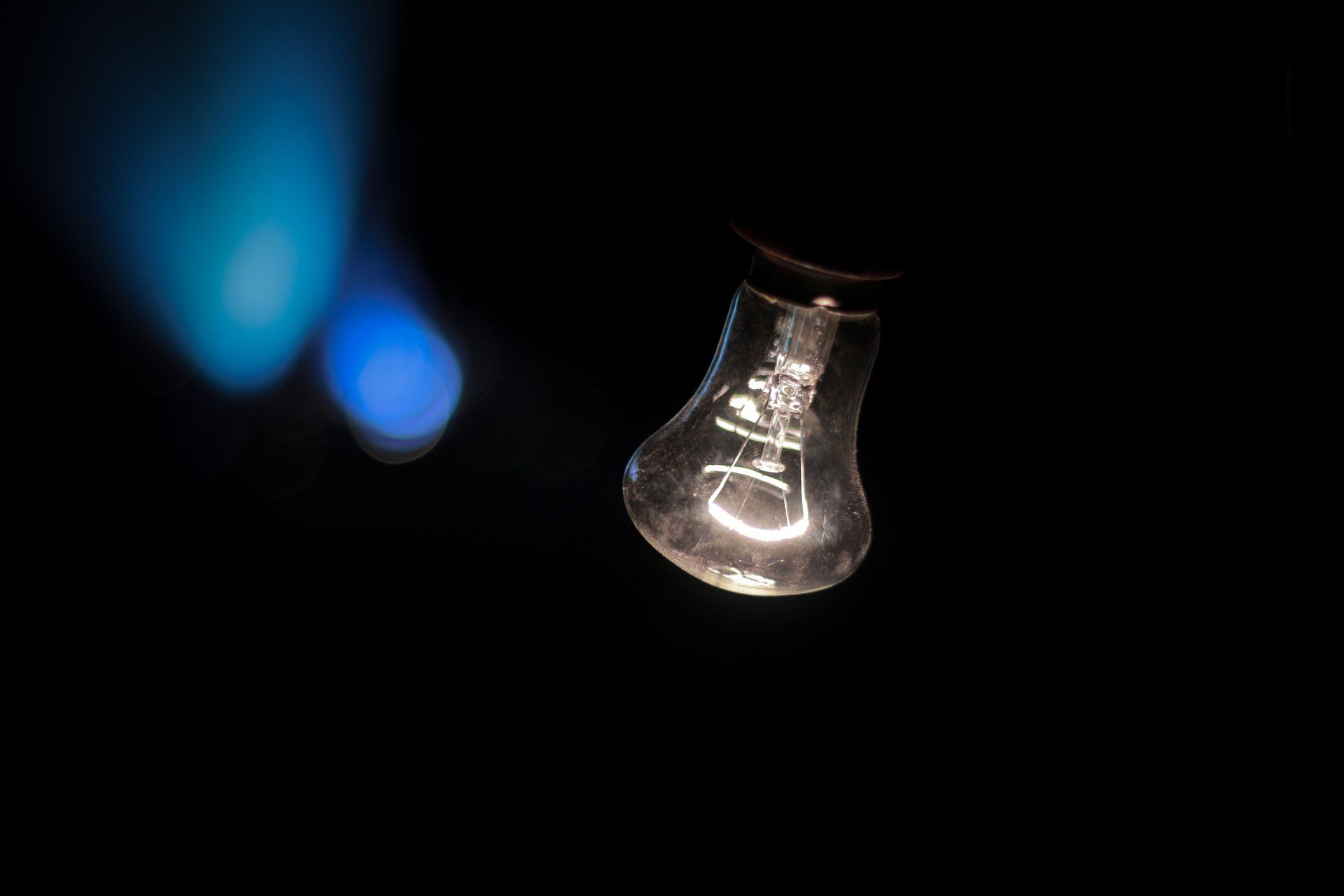 An incandescent light bulb is hanging from a ceiling in the dark.