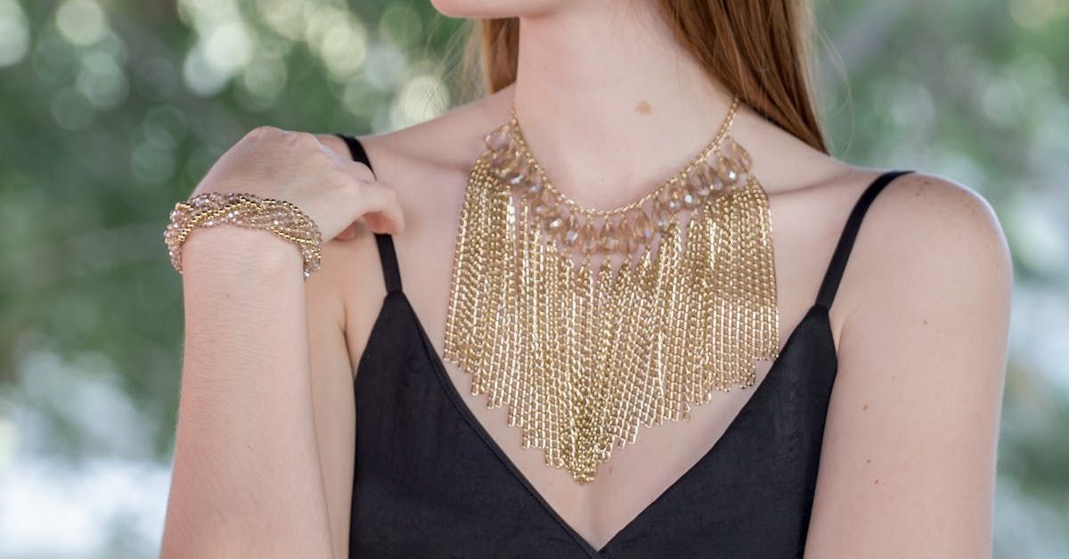 a woman in a black dress is wearing a gold necklace and bracelet .