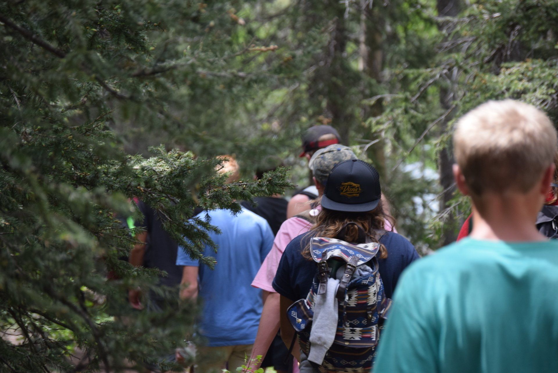 Hikers walking through a forest with backpacks and hats, on a trail path.