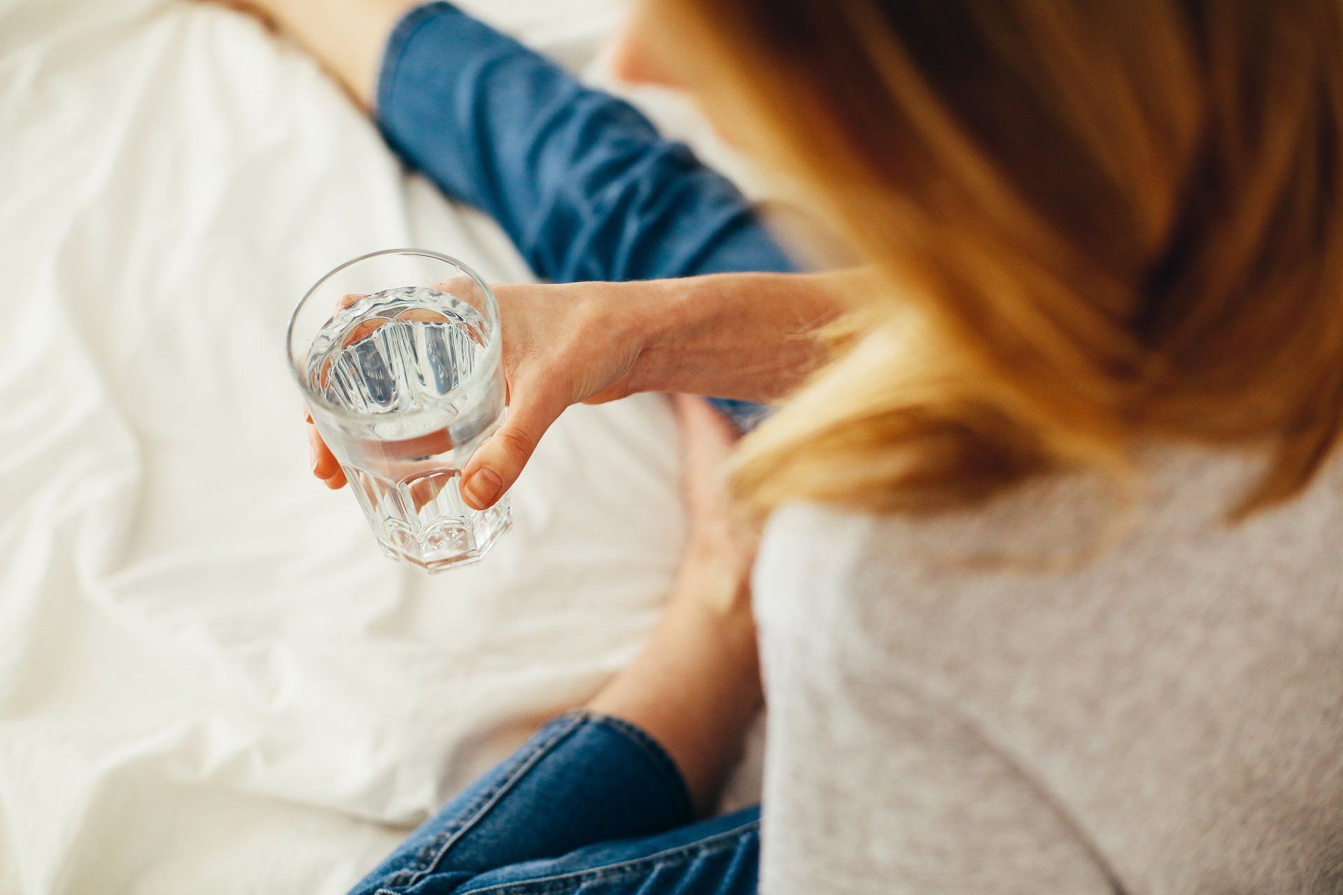 A woman is sitting on a bed holding a glass of water.
