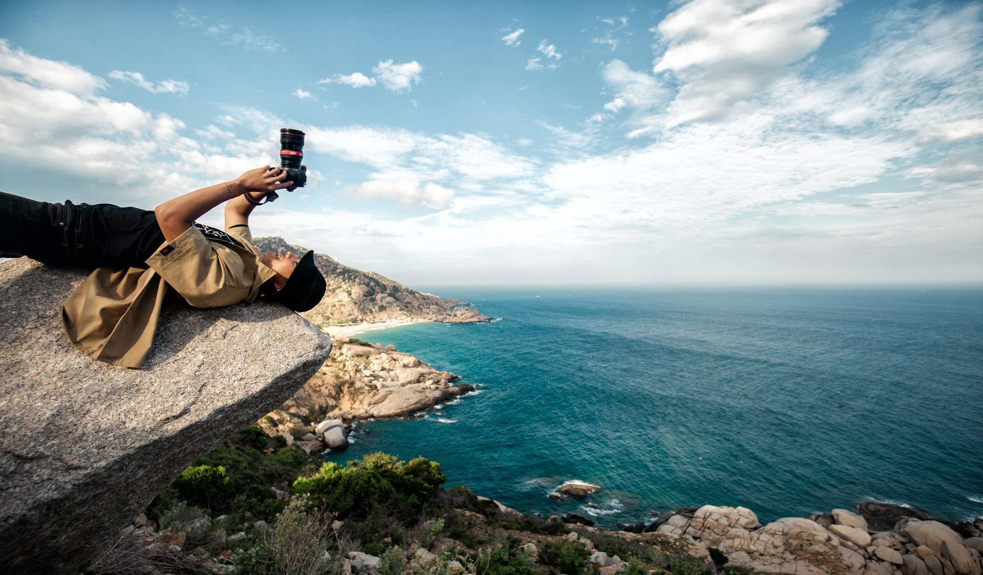une personne allongée sur un rocher tenant un appareil photo avec l' océan en arrière-plan