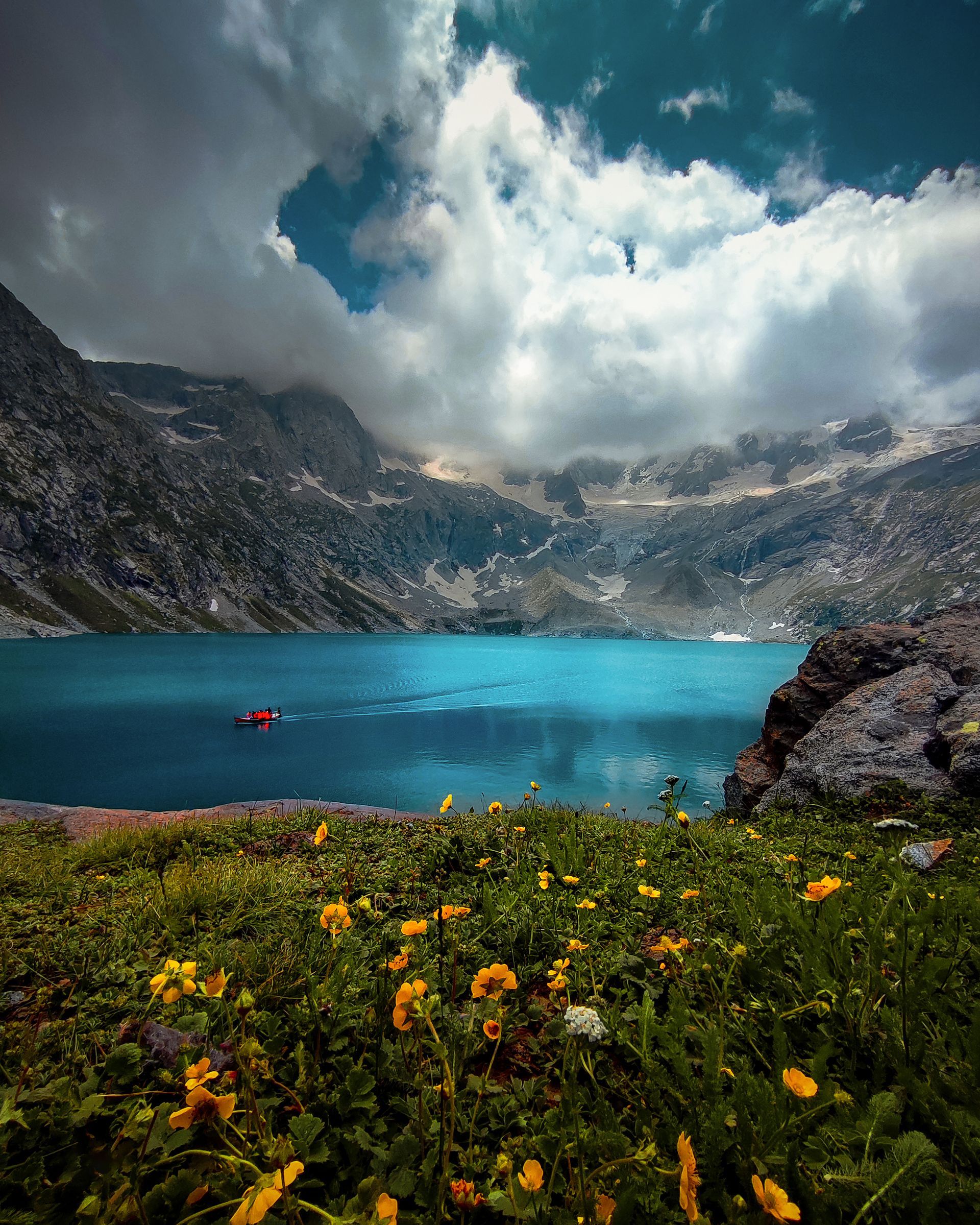 A lake surrounded by mountains and flowers with a boat in the water.