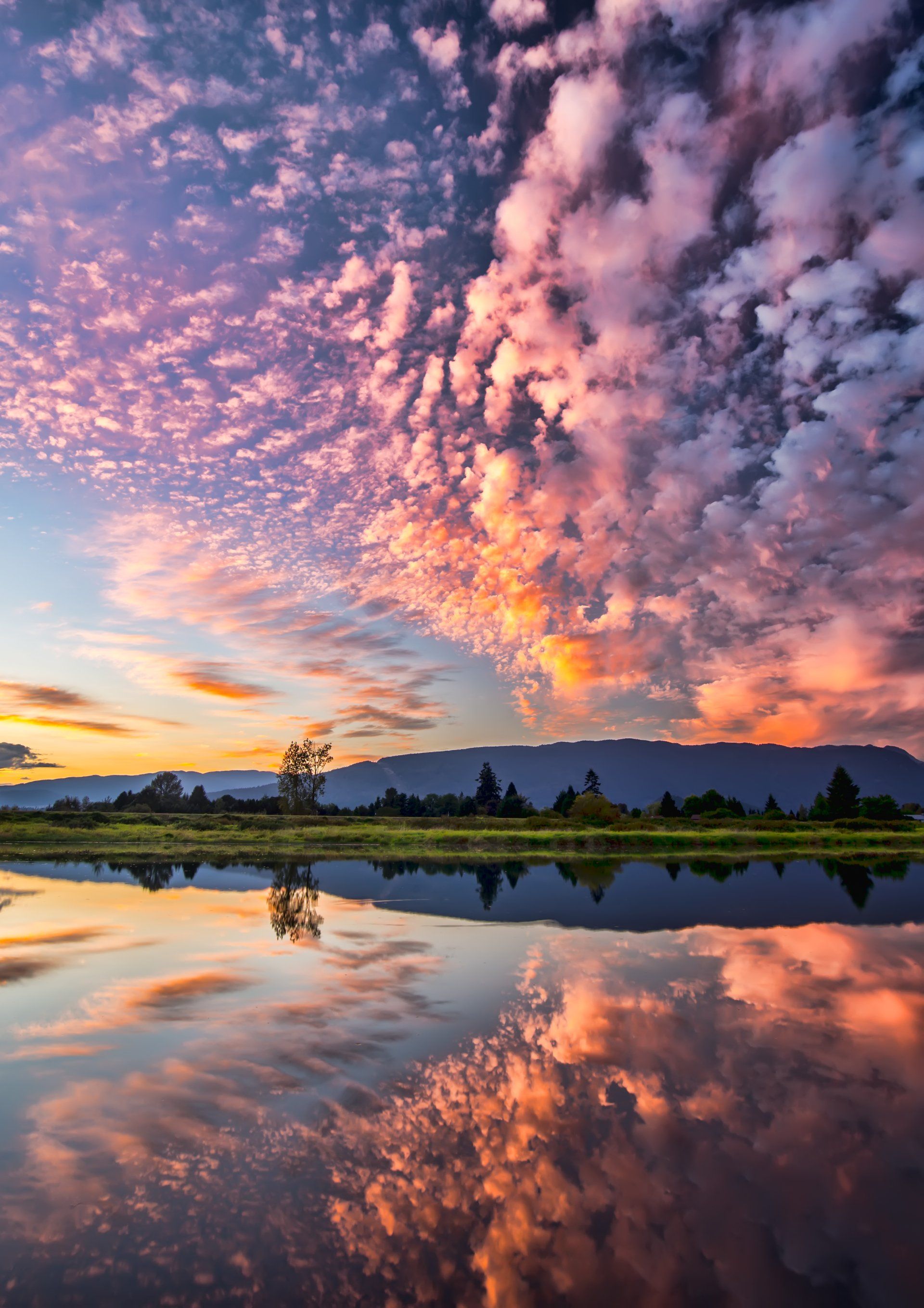 a sunset over a lake with mountains in the background and clouds reflected in the water .