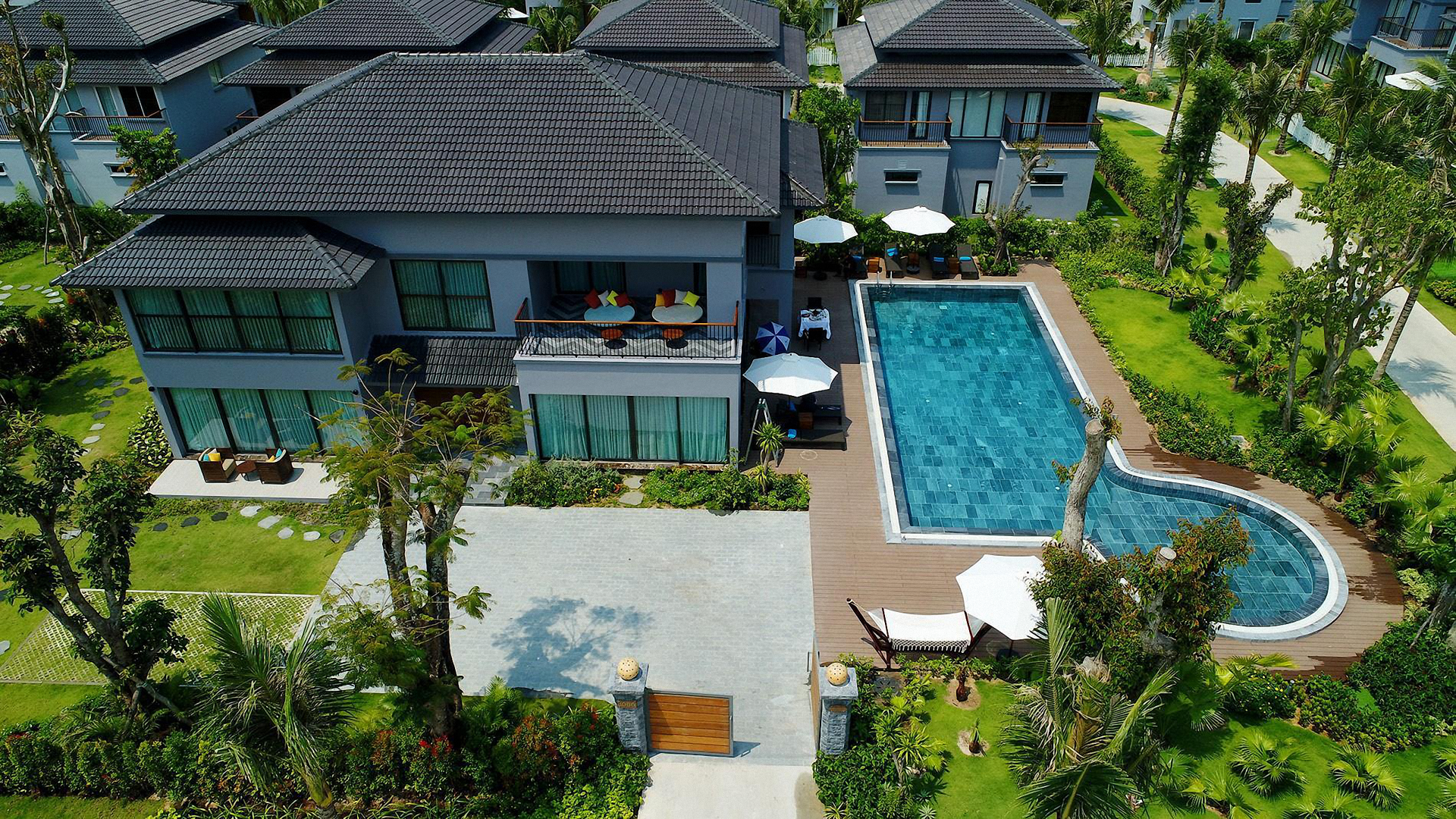 An aerial view of a large house with a large swimming pool surrounded by trees.