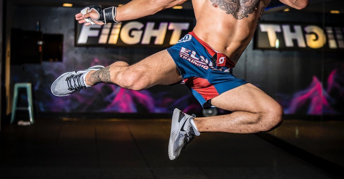 A shirtless man is jumping in the air in a gym.