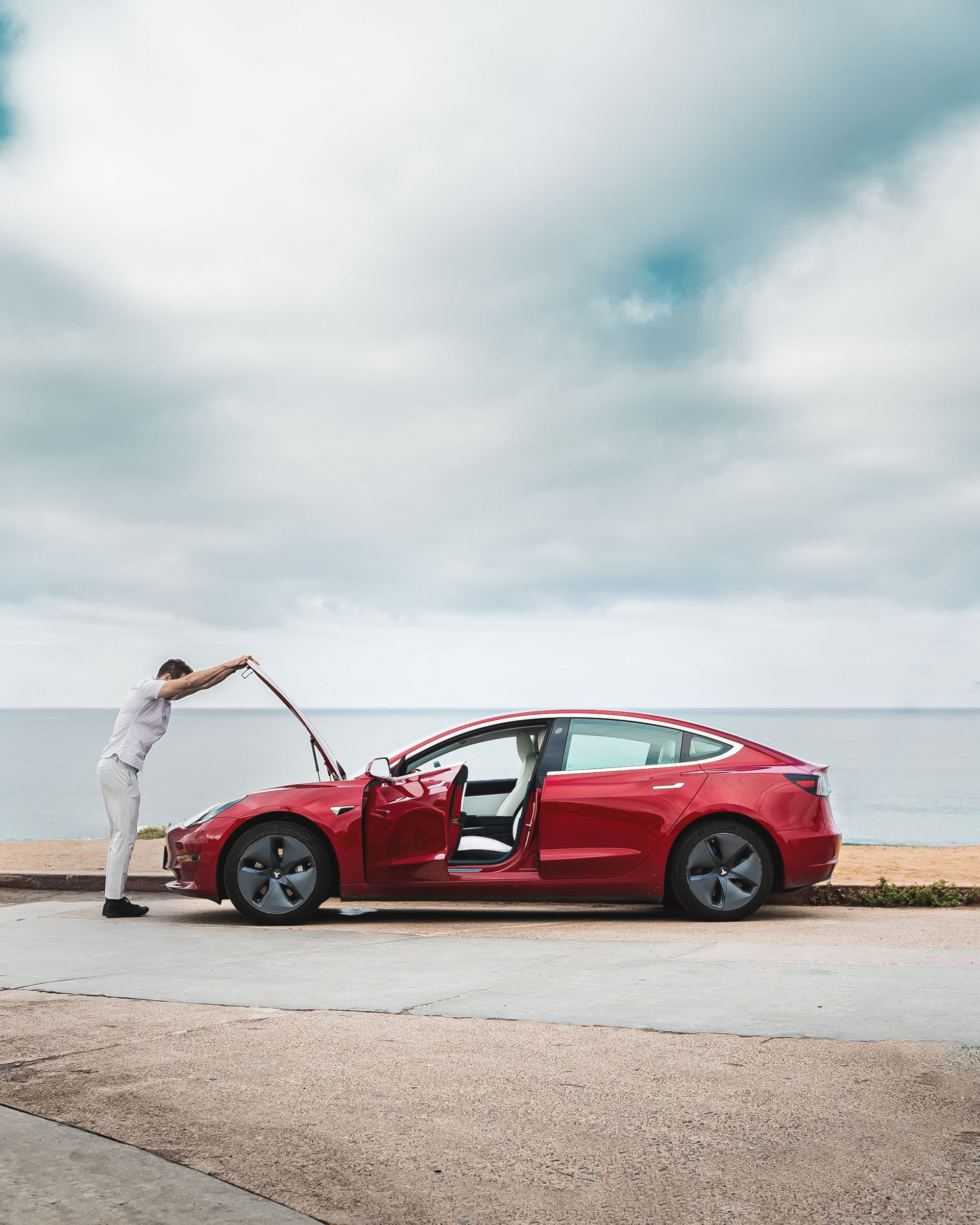 A man is opening the hood of a red tesla  | Chicoine & Sons Automotive