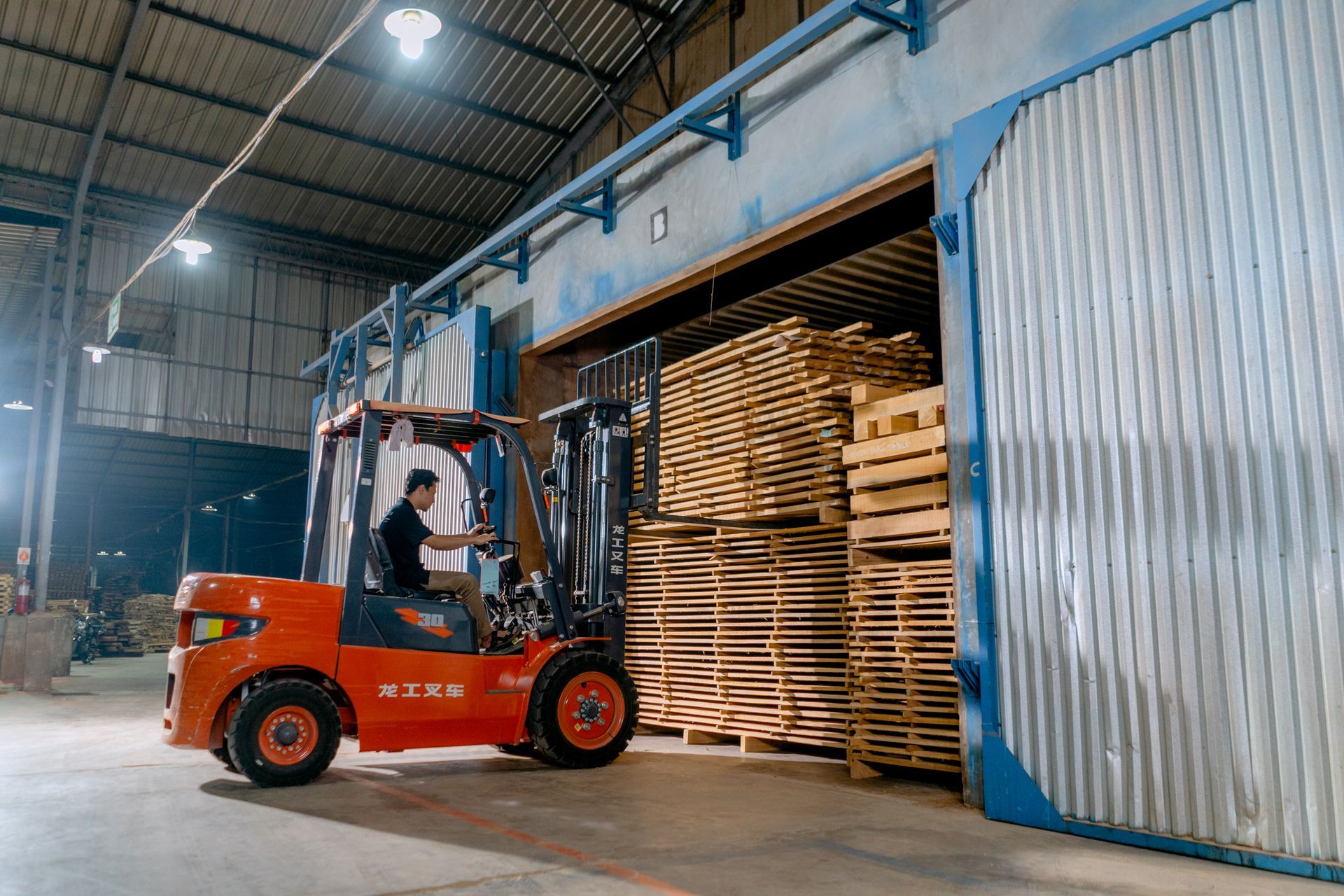 A man is driving a forklift in a warehouse filled with wooden pallets.