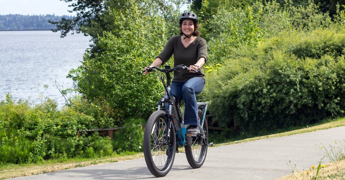 A woman is riding an electric bike on a path next to a body of water.