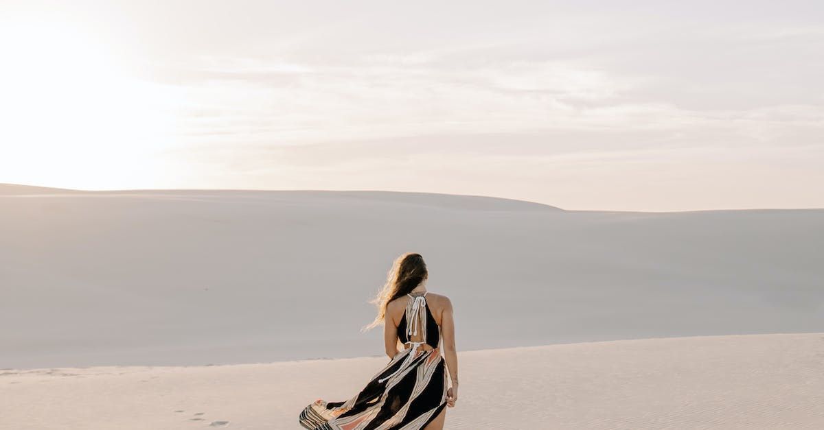 Uma mulher com um vestido preto e branco está caminhando em uma praia arenosa.