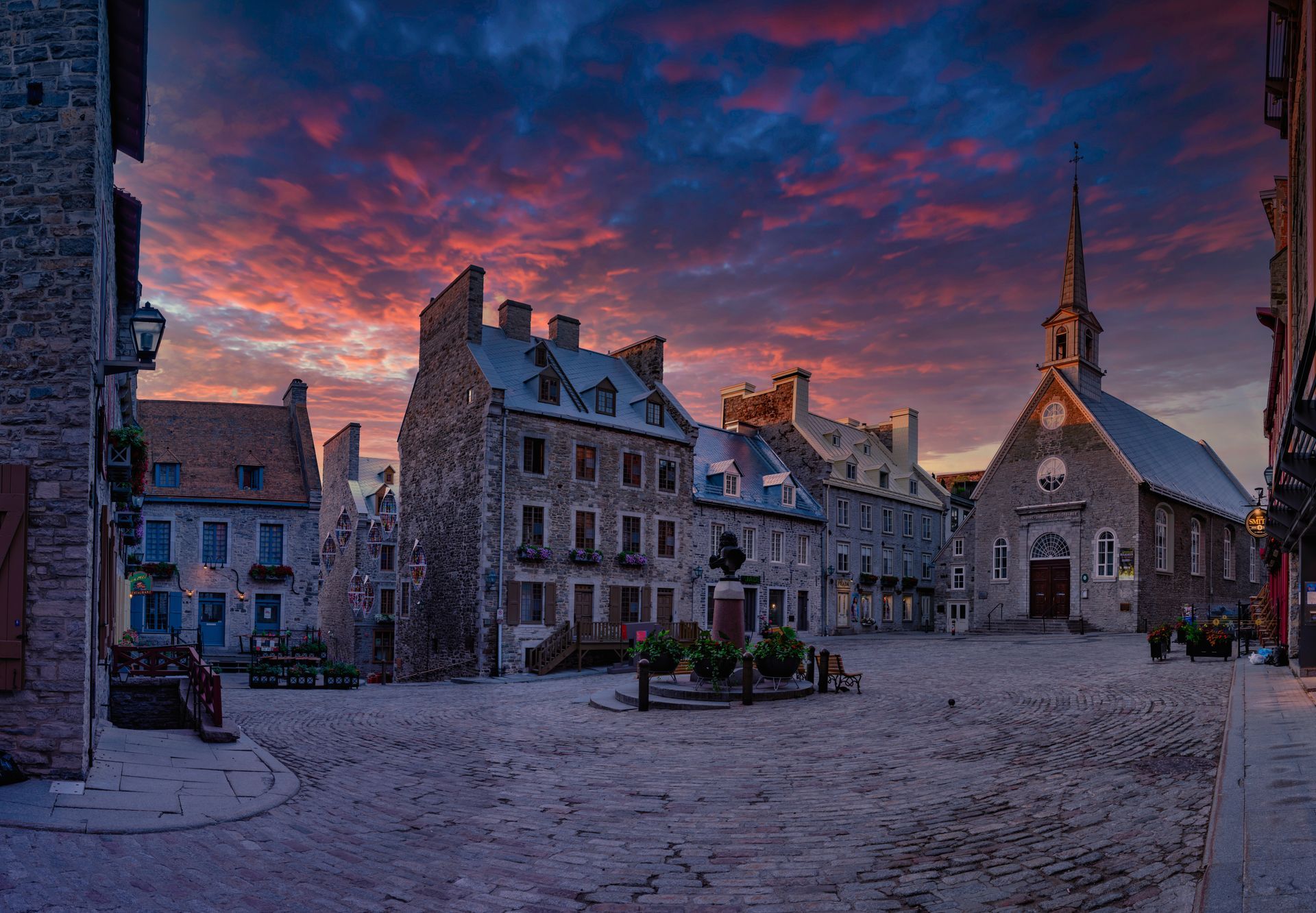 There is a church in the middle of a square with a sunset in the background in Quebec City.