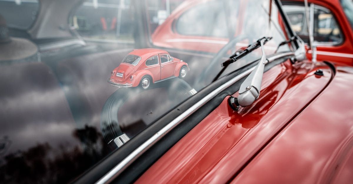 A red car with a toy car reflected in the windshield.
