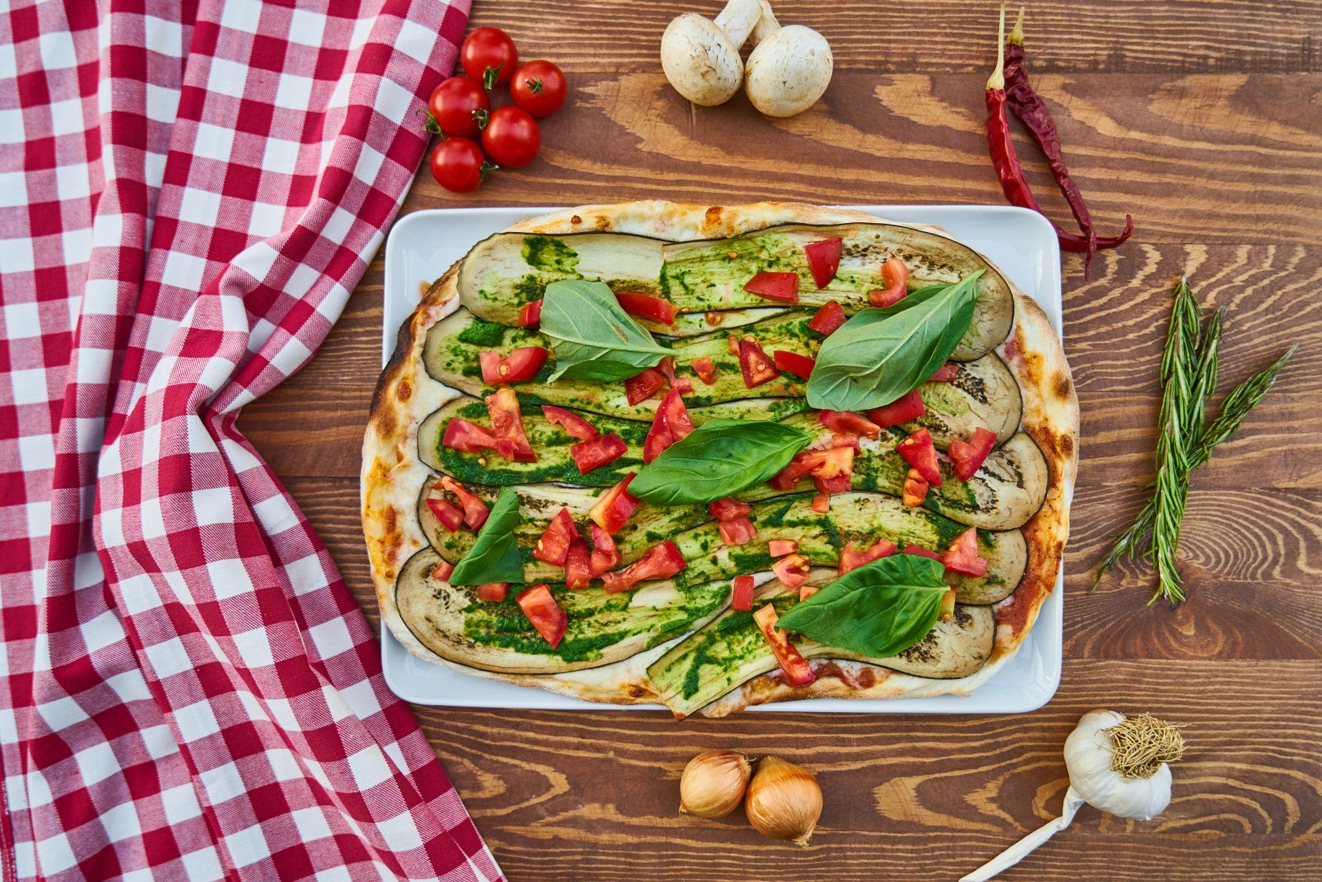 A pizza with vegetables on a white plate on a wooden table.