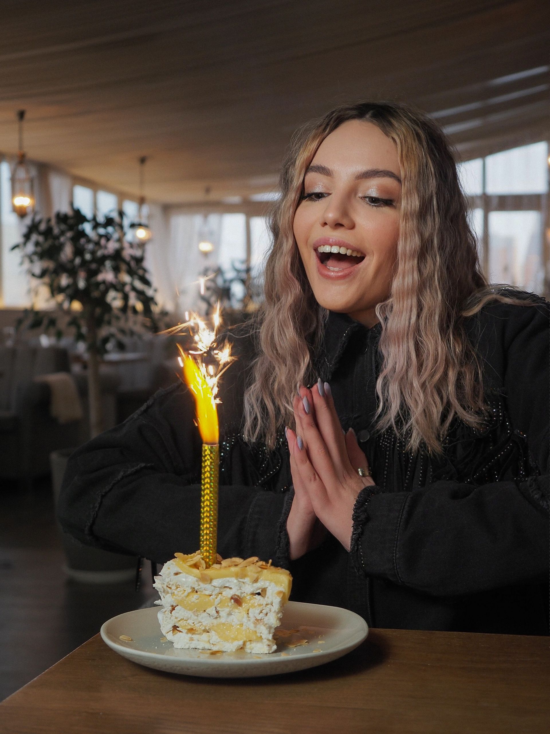 Woman blowing out a birthday candle on a small cake in a restaurant, smiling with excitement.
