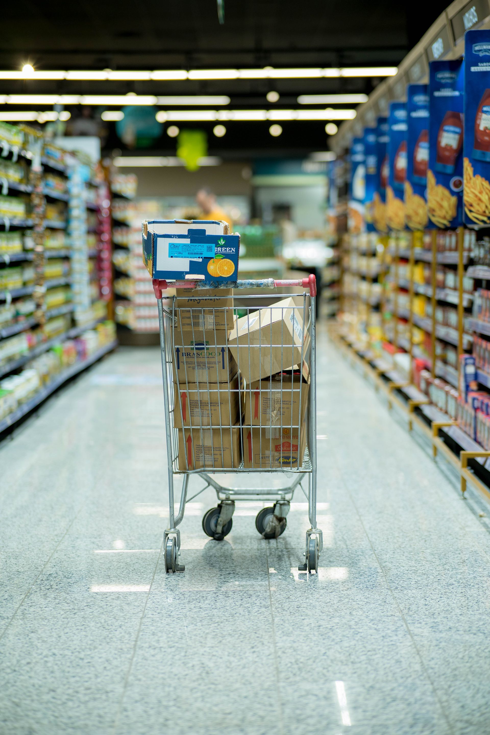 A shopping cart is filled with boxes in a supermarket aisle.