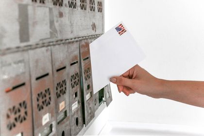 A person is putting an envelope in a mailbox with an american flag stamp